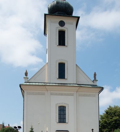 Zdjęcie nr 13: Kościół murowany, tynkowany, na kamiennym podmurowaniu, orientowany, jednonawowy. Prezbiterium prostokątne, krótkie, zamknięte trójbocznie, przy południowej ścianie prostokątna zakrystia z piętrem, z prostokątnym aneksem od zachodu. Nawa główna szersza od prezbiterium, na rzucie prostokąta, od zachodu przylega prostokątny przedsionek z wieżą na planie kwadratu. Wnętrze podzielone na cztery prostokątne przęsła i absydę, wydzielone arkadami, z gurtami spływającymi na zwielokrotnione pilastry. Każde przęsło nakryte sklepieniem o zaokrąglonych narożach. Łuk tęczowy półkolisty. W zachodniej części parapet chóru muzycznego wsparty na dwóch filarach i dwóch półfilarach, tworzących trzy arkady. Fasada trójosiowa, z wbudowaną wieżą, ujętą spłaszczonymi spływami zakończonymi cokołami z figurami. Osie wydzielone lizenami, podtrzymującymi profilowany gzyms, pod nim malowany fryz z dekoracją roślinną. Na osi portal w formie stojącego prostokąta zamkniętego łukiem odcinkowym, ujęty opaską tynkową, zakończoną kluczem. Drzwi drewniane, dwuskrzydłowe. Nad portalem fragment profilowanego gzymsu z daszkiem okapowym. Powyżej, na osi okno w formie stojącego prostokąta zamkniętego łukiem odcinkowym, w profilowanej opasce tynkowej, ujętej malowaną dekoracją geometryczną. Wieża dwukondygnacyjna, flankowana w narożach lizenami podtrzymującymi profilowany gzyms wieńczący. Na ścianie frontowej dwa okna na każdej kondygnacji, w formie stojącego prostokąta zamkniętego łukiem odcinkowym, w profilowanej opasce tynkowej, otoczonej malowaną dekoracją geometryczną, zwieńczone tarczą zegarową. Na pozostałych trzech ścianach wieży po jednym analogicznym oknie w drugiej kondygnacji i tarczy zegarowej. Elewacje północna i południowa artykułowane lizenami podtrzymującymi profilowany gzyms, z dekoracyjnym fryzem poniżej. Okna w formie stojącego prostokąta zamkniętego łukiem odcinkowym, w profilowanej opasce tynkowej z kluczem, ujętej malowaną dekoracją geometryczną: cztery w północnej i trzy w południowej. W zakrystii jedno prostokątne okno od południa i dwa w każdej kondygnacji od wschodu. Nawa główna i prezbiterium nakryte osobnymi dachami dwuspadowymi. Na ich połączeniu wieżyczka na sygnaturkę z latarnią, zwieńczona hełmem baniastym z krzyżem. Wieża nakryta hełmem baniastym zakończonym kulą z krzyżem. Zakrystia przykryta dachem trójspadowym, a aneks czterospadowym. 