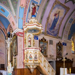 Zdjęcie nr 1: Ambona przyścienna, wisząca, z wejściem schodami od strony prezbiterium. Kosz jest na planie sześcioboku ze ściankami wydzielonymi pilastrami o trzonach w formie spływów wolutowych, zdobionych motywem  kampanuli i cekinów. Pola ścianek wypełniają płyciny w kształcie stojącego prostokąta dołem zamkniętego gzymsem,  górą łukiem wklęsło-wypukłym w formie ornamentu rocaille’owego. Umieszczono w nich płaskorzeźbione wizerunki czterech ewangelistów ukazanych w półpostaci. W dłoniach trzymają księgi lub zwoje oraz narzędzia pisarskie. U dołu każdej postaci znajduje się banderola z napisami (od lewej: „Św(ięty) Jan, Św(ięty) Łukasz, Św(ięty) Marek, Św(ięty) Mateusz”). Podstawę kosza obiega półwałek, natomiast podwieszenie, ujęte sześcioma spływami wolutowymi, zakończone jest dekoracyjną szyszką w kształcie osłoniętej liśćmi kiści winnej latorośli. Parapet ma formę pełnego belkowania wyłamującego się ponad wspierającymi go pilastrami.  Prowadzące na ambonę schody są jednobiegowe, z balustradą w formie ścianki zdobionej 4 płycinami w kształcie stojących prostokątów zamkniętych górą i dołem ornamentyką rocaille’ową, ujętej na końcu spływem wolutowym. Flankowany parą ażurowych, ornamentowych uszaków zaplecek wypełnia płycina w kształcie stojącego prostokąta zamkniętego łukiem wklęsło-wypukłym z płaskorzeźbionym, całopostaciowym przedstawieniem Chrystusa Dobrego Pasterza. Baldachim jest na rzucie ośmioboku, jego podstawę obiega wyłamujące się na narożach belkowanie, którego dolną krawędź zdobi motyw lambrekinu, natomiast górną kartusze rocaille’owe z kratką regencyjną. W podniebiu polichromowany motyw pokrytego obłokami nieba z płaskorzeźbioną gołębicą Ducha Świętego pośrodku. Naroża baldachimu ujmują spływy wolutowe pokryte ornamentem cekinowym. Zwieńczenie ma formę kopuły, na której osadzona jest figura dmącego w złoconą trąbę archanioła Michała stojącego na niebieskiej, ugwieżdżonej kuli, dołem ujętej wieńcem srebrzonymi obłoków. 
Struktura ambony utrzymana jest w kolorze białym, pola płycin są marmoryzowane w odcieniach kremowym i pomarańczowym, detal architektoniczny i ornamentyka są złocone i srebrzone oraz w kolorze bordowym.
