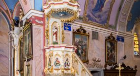 Zdjęcie nr 1: Ambona przyścienna, wisząca, z wejściem schodami od strony prezbiterium. Kosz jest na planie sześcioboku ze ściankami wydzielonymi pilastrami o trzonach w formie spływów wolutowych, zdobionych motywem  kampanuli i cekinów. Pola ścianek wypełniają płyciny w kształcie stojącego prostokąta dołem zamkniętego gzymsem,  górą łukiem wklęsło-wypukłym w formie ornamentu rocaille’owego. Umieszczono w nich płaskorzeźbione wizerunki czterech ewangelistów ukazanych w półpostaci. W dłoniach trzymają księgi lub zwoje oraz narzędzia pisarskie. U dołu każdej postaci znajduje się banderola z napisami (od lewej: „Św(ięty) Jan, Św(ięty) Łukasz, Św(ięty) Marek, Św(ięty) Mateusz”). Podstawę kosza obiega półwałek, natomiast podwieszenie, ujęte sześcioma spływami wolutowymi, zakończone jest dekoracyjną szyszką w kształcie osłoniętej liśćmi kiści winnej latorośli. Parapet ma formę pełnego belkowania wyłamującego się ponad wspierającymi go pilastrami.  Prowadzące na ambonę schody są jednobiegowe, z balustradą w formie ścianki zdobionej 4 płycinami w kształcie stojących prostokątów zamkniętych górą i dołem ornamentyką rocaille’ową, ujętej na końcu spływem wolutowym. Flankowany parą ażurowych, ornamentowych uszaków zaplecek wypełnia płycina w kształcie stojącego prostokąta zamkniętego łukiem wklęsło-wypukłym z płaskorzeźbionym, całopostaciowym przedstawieniem Chrystusa Dobrego Pasterza. Baldachim jest na rzucie ośmioboku, jego podstawę obiega wyłamujące się na narożach belkowanie, którego dolną krawędź zdobi motyw lambrekinu, natomiast górną kartusze rocaille’owe z kratką regencyjną. W podniebiu polichromowany motyw pokrytego obłokami nieba z płaskorzeźbioną gołębicą Ducha Świętego pośrodku. Naroża baldachimu ujmują spływy wolutowe pokryte ornamentem cekinowym. Zwieńczenie ma formę kopuły, na której osadzona jest figura dmącego w złoconą trąbę archanioła Michała stojącego na niebieskiej, ugwieżdżonej kuli, dołem ujętej wieńcem srebrzonymi obłoków. 
Struktura ambony utrzymana jest w kolorze białym, pola płycin są marmoryzowane w odcieniach kremowym i pomarańczowym, detal architektoniczny i ornamentyka są złocone i srebrzone oraz w kolorze bordowym.
