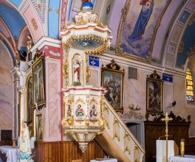 Zdjęcie nr 1: Ambona przyścienna, wisząca, z wejściem schodami od strony prezbiterium. Kosz jest na planie sześcioboku ze ściankami wydzielonymi pilastrami o trzonach w formie spływów wolutowych, zdobionych motywem  kampanuli i cekinów. Pola ścianek wypełniają płyciny w kształcie stojącego prostokąta dołem zamkniętego gzymsem,  górą łukiem wklęsło-wypukłym w formie ornamentu rocaille’owego. Umieszczono w nich płaskorzeźbione wizerunki czterech ewangelistów ukazanych w półpostaci. W dłoniach trzymają księgi lub zwoje oraz narzędzia pisarskie. U dołu każdej postaci znajduje się banderola z napisami (od lewej: „Św(ięty) Jan, Św(ięty) Łukasz, Św(ięty) Marek, Św(ięty) Mateusz”). Podstawę kosza obiega półwałek, natomiast podwieszenie, ujęte sześcioma spływami wolutowymi, zakończone jest dekoracyjną szyszką w kształcie osłoniętej liśćmi kiści winnej latorośli. Parapet ma formę pełnego belkowania wyłamującego się ponad wspierającymi go pilastrami.  Prowadzące na ambonę schody są jednobiegowe, z balustradą w formie ścianki zdobionej 4 płycinami w kształcie stojących prostokątów zamkniętych górą i dołem ornamentyką rocaille’ową, ujętej na końcu spływem wolutowym. Flankowany parą ażurowych, ornamentowych uszaków zaplecek wypełnia płycina w kształcie stojącego prostokąta zamkniętego łukiem wklęsło-wypukłym z płaskorzeźbionym, całopostaciowym przedstawieniem Chrystusa Dobrego Pasterza. Baldachim jest na rzucie ośmioboku, jego podstawę obiega wyłamujące się na narożach belkowanie, którego dolną krawędź zdobi motyw lambrekinu, natomiast górną kartusze rocaille’owe z kratką regencyjną. W podniebiu polichromowany motyw pokrytego obłokami nieba z płaskorzeźbioną gołębicą Ducha Świętego pośrodku. Naroża baldachimu ujmują spływy wolutowe pokryte ornamentem cekinowym. Zwieńczenie ma formę kopuły, na której osadzona jest figura dmącego w złoconą trąbę archanioła Michała stojącego na niebieskiej, ugwieżdżonej kuli, dołem ujętej wieńcem srebrzonymi obłoków. 
Struktura ambony utrzymana jest w kolorze białym, pola płycin są marmoryzowane w odcieniach kremowym i pomarańczowym, detal architektoniczny i ornamentyka są złocone i srebrzone oraz w kolorze bordowym.

