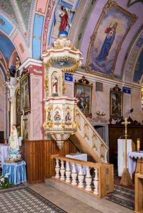 Zdjęcie nr 1: Ambona przyścienna, wisząca, z wejściem schodami od strony prezbiterium. Kosz jest na planie sześcioboku ze ściankami wydzielonymi pilastrami o trzonach w formie spływów wolutowych, zdobionych motywem  kampanuli i cekinów. Pola ścianek wypełniają płyciny w kształcie stojącego prostokąta dołem zamkniętego gzymsem,  górą łukiem wklęsło-wypukłym w formie ornamentu rocaille’owego. Umieszczono w nich płaskorzeźbione wizerunki czterech ewangelistów ukazanych w półpostaci. W dłoniach trzymają księgi lub zwoje oraz narzędzia pisarskie. U dołu każdej postaci znajduje się banderola z napisami (od lewej: „Św(ięty) Jan, Św(ięty) Łukasz, Św(ięty) Marek, Św(ięty) Mateusz”). Podstawę kosza obiega półwałek, natomiast podwieszenie, ujęte sześcioma spływami wolutowymi, zakończone jest dekoracyjną szyszką w kształcie osłoniętej liśćmi kiści winnej latorośli. Parapet ma formę pełnego belkowania wyłamującego się ponad wspierającymi go pilastrami.  Prowadzące na ambonę schody są jednobiegowe, z balustradą w formie ścianki zdobionej 4 płycinami w kształcie stojących prostokątów zamkniętych górą i dołem ornamentyką rocaille’ową, ujętej na końcu spływem wolutowym. Flankowany parą ażurowych, ornamentowych uszaków zaplecek wypełnia płycina w kształcie stojącego prostokąta zamkniętego łukiem wklęsło-wypukłym z płaskorzeźbionym, całopostaciowym przedstawieniem Chrystusa Dobrego Pasterza. Baldachim jest na rzucie ośmioboku, jego podstawę obiega wyłamujące się na narożach belkowanie, którego dolną krawędź zdobi motyw lambrekinu, natomiast górną kartusze rocaille’owe z kratką regencyjną. W podniebiu polichromowany motyw pokrytego obłokami nieba z płaskorzeźbioną gołębicą Ducha Świętego pośrodku. Naroża baldachimu ujmują spływy wolutowe pokryte ornamentem cekinowym. Zwieńczenie ma formę kopuły, na której osadzona jest figura dmącego w złoconą trąbę archanioła Michała stojącego na niebieskiej, ugwieżdżonej kuli, dołem ujętej wieńcem srebrzonymi obłoków. 
Struktura ambony utrzymana jest w kolorze białym, pola płycin są marmoryzowane w odcieniach kremowym i pomarańczowym, detal architektoniczny i ornamentyka są złocone i srebrzone oraz w kolorze bordowym.
