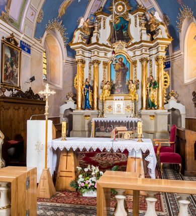 Zdjęcie nr 5: Ołtarz architektoniczny, jednokondygnacyjny, jednoosiowy, ze zwieńczeniem. Ołtarz murowany, prostopadłościenny z antepedium w formie prostokątnego obrazu ze sceną Ostatniej Wieczerzy według fresku Leonarda da Vinci. Na mensie tabernakulum w formie prostopadłościennej skrzyni osadzonej na niewielkim cokole i zwieńczonej gzymsem zdobionym wicią winnej latorośli. Metalowe drzwiczki w kształcie stojącego prostokąta z płyciną z motywem kielicha eucharystycznego, po bokach zdobione wicią winnej latorośli, flankowane parą prostokątnych płycin z motywami płaskorzeźbionych, uskrzydlonych główek anielskich. Na tabernakulum po bokach para figur klęczących aniołów w długich, złoconych sukniach. Retabulum osadzone na wysokim zryzalitowanym ukośnie po bokach cokole. Część środkowa ujęta dwoma parami kolumn ustawionych na tle dwóch par filarów, z czego skrajne bardziej wysunięte. Podpory wspierają wyłamujące się ponad nimi przerwane belkowanie. Zwieńczenie ujęte parą ukośnie ustawionych spływów wolutowych, zamknięte łukiem odcinkowym, flankowane przerwanym wolutowym przyczółkiem. Po bokach retabulum para bramek o przejściach zamkniętych łukami kotarowymi, zwieńczonych fragmentami gzymsów w postaci łuków wklęsło-wypukłych. Trzony filarów zdobione kampanulami, fryz rozetami. Retabulum ujmuje para ażurowych uszaków. Pośrodku przerwanego belkowania monogram maryjny. Pola spływów wolutowych zwieńczenia zdobią motywy kampanuli, szczyt w formie promienistej glorii z okiem Opatrzności pośrodku ujętym kręgiem obłoków. Na przerwanym przyczółku para figur siedzących aniołów w długich, złoconych sukniach. Pole części środkowej w kształcie stojącego prostokąta zamkniętego półkolistym łukiem nadwieszonym z uskokami, ujęte profilowaną, złoconą ramą. W środku obraz Matki Boskiej Pocieszenia, na zasuwie wizerunek św. Jakuba Starszego. Po bokach, między kolumnami para figur, po prawej stronie św. Paweł, po lewej św. Piotr. W zwieńczeniu obraz w kształcie trapezu o wklęsłych ramionach i podstawie, ściętych narożach dolnych, zamknięty łukiem wklęsło-wypukłym z przedstawieniem stygmatyzacji św. Franciszka. Struktura polichromowana w kolorze białym, częściowo marmoryzowana w odcieniach beżów, detal architektoniczny i ornamentyka złocone, marmoryzowane i srebrzone.     