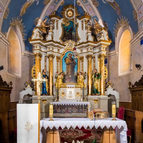 Zdjęcie nr 1: Ołtarz architektoniczny, jednokondygnacyjny, jednoosiowy, ze zwieńczeniem. Ołtarz murowany, prostopadłościenny z antepedium w formie prostokątnego obrazu ze sceną Ostatniej Wieczerzy według fresku Leonarda da Vinci. Na mensie tabernakulum w formie prostopadłościennej skrzyni osadzonej na niewielkim cokole i zwieńczonej gzymsem zdobionym wicią winnej latorośli. Metalowe drzwiczki w kształcie stojącego prostokąta z płyciną z motywem kielicha eucharystycznego, po bokach zdobione wicią winnej latorośli, flankowane parą prostokątnych płycin z motywami płaskorzeźbionych, uskrzydlonych główek anielskich. Na tabernakulum po bokach para figur klęczących aniołów w długich, złoconych sukniach. Retabulum osadzone na wysokim zryzalitowanym ukośnie po bokach cokole. Część środkowa ujęta dwoma parami kolumn ustawionych na tle dwóch par filarów, z czego skrajne bardziej wysunięte. Podpory wspierają wyłamujące się ponad nimi przerwane belkowanie. Zwieńczenie ujęte parą ukośnie ustawionych spływów wolutowych, zamknięte łukiem odcinkowym, flankowane przerwanym wolutowym przyczółkiem. Po bokach retabulum para bramek o przejściach zamkniętych łukami kotarowymi, zwieńczonych fragmentami gzymsów w postaci łuków wklęsło-wypukłych. Trzony filarów zdobione kampanulami, fryz rozetami. Retabulum ujmuje para ażurowych uszaków. Pośrodku przerwanego belkowania monogram maryjny. Pola spływów wolutowych zwieńczenia zdobią motywy kampanuli, szczyt w formie promienistej glorii z okiem Opatrzności pośrodku ujętym kręgiem obłoków. Na przerwanym przyczółku para figur siedzących aniołów w długich, złoconych sukniach. Pole części środkowej w kształcie stojącego prostokąta zamkniętego półkolistym łukiem nadwieszonym z uskokami, ujęte profilowaną, złoconą ramą. W środku obraz Matki Boskiej Pocieszenia, na zasuwie wizerunek św. Jakuba Starszego. Po bokach, między kolumnami para figur, po prawej stronie św. Paweł, po lewej św. Piotr. W zwieńczeniu obraz w kształcie trapezu o wklęsłych ramionach i podstawie, ściętych narożach dolnych, zamknięty łukiem wklęsło-wypukłym z przedstawieniem stygmatyzacji św. Franciszka. Struktura polichromowana w kolorze białym, częściowo marmoryzowana w odcieniach beżów, detal architektoniczny i ornamentyka złocone, marmoryzowane i srebrzone.     