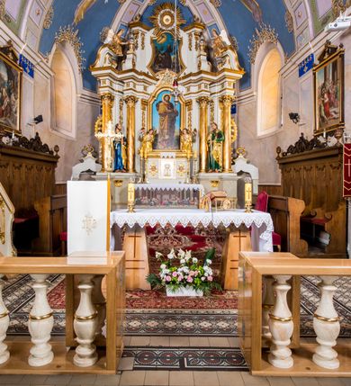 Zdjęcie nr 6: Ołtarz architektoniczny, jednokondygnacyjny, jednoosiowy, ze zwieńczeniem. Ołtarz murowany, prostopadłościenny z antepedium w formie prostokątnego obrazu ze sceną Ostatniej Wieczerzy według fresku Leonarda da Vinci. Na mensie tabernakulum w formie prostopadłościennej skrzyni osadzonej na niewielkim cokole i zwieńczonej gzymsem zdobionym wicią winnej latorośli. Metalowe drzwiczki w kształcie stojącego prostokąta z płyciną z motywem kielicha eucharystycznego, po bokach zdobione wicią winnej latorośli, flankowane parą prostokątnych płycin z motywami płaskorzeźbionych, uskrzydlonych główek anielskich. Na tabernakulum po bokach para figur klęczących aniołów w długich, złoconych sukniach. Retabulum osadzone na wysokim zryzalitowanym ukośnie po bokach cokole. Część środkowa ujęta dwoma parami kolumn ustawionych na tle dwóch par filarów, z czego skrajne bardziej wysunięte. Podpory wspierają wyłamujące się ponad nimi przerwane belkowanie. Zwieńczenie ujęte parą ukośnie ustawionych spływów wolutowych, zamknięte łukiem odcinkowym, flankowane przerwanym wolutowym przyczółkiem. Po bokach retabulum para bramek o przejściach zamkniętych łukami kotarowymi, zwieńczonych fragmentami gzymsów w postaci łuków wklęsło-wypukłych. Trzony filarów zdobione kampanulami, fryz rozetami. Retabulum ujmuje para ażurowych uszaków. Pośrodku przerwanego belkowania monogram maryjny. Pola spływów wolutowych zwieńczenia zdobią motywy kampanuli, szczyt w formie promienistej glorii z okiem Opatrzności pośrodku ujętym kręgiem obłoków. Na przerwanym przyczółku para figur siedzących aniołów w długich, złoconych sukniach. Pole części środkowej w kształcie stojącego prostokąta zamkniętego półkolistym łukiem nadwieszonym z uskokami, ujęte profilowaną, złoconą ramą. W środku obraz Matki Boskiej Pocieszenia, na zasuwie wizerunek św. Jakuba Starszego. Po bokach, między kolumnami para figur, po prawej stronie św. Paweł, po lewej św. Piotr. W zwieńczeniu obraz w kształcie trapezu o wklęsłych ramionach i podstawie, ściętych narożach dolnych, zamknięty łukiem wklęsło-wypukłym z przedstawieniem stygmatyzacji św. Franciszka. Struktura polichromowana w kolorze białym, częściowo marmoryzowana w odcieniach beżów, detal architektoniczny i ornamentyka złocone, marmoryzowane i srebrzone.     