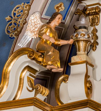 Zdjęcie nr 18: Ołtarz architektoniczny, jednokondygnacyjny, jednoosiowy, ze zwieńczeniem. Ołtarz murowany, prostopadłościenny z antepedium w formie prostokątnego obrazu ze sceną Ostatniej Wieczerzy według fresku Leonarda da Vinci. Na mensie tabernakulum w formie prostopadłościennej skrzyni osadzonej na niewielkim cokole i zwieńczonej gzymsem zdobionym wicią winnej latorośli. Metalowe drzwiczki w kształcie stojącego prostokąta z płyciną z motywem kielicha eucharystycznego, po bokach zdobione wicią winnej latorośli, flankowane parą prostokątnych płycin z motywami płaskorzeźbionych, uskrzydlonych główek anielskich. Na tabernakulum po bokach para figur klęczących aniołów w długich, złoconych sukniach. Retabulum osadzone na wysokim zryzalitowanym ukośnie po bokach cokole. Część środkowa ujęta dwoma parami kolumn ustawionych na tle dwóch par filarów, z czego skrajne bardziej wysunięte. Podpory wspierają wyłamujące się ponad nimi przerwane belkowanie. Zwieńczenie ujęte parą ukośnie ustawionych spływów wolutowych, zamknięte łukiem odcinkowym, flankowane przerwanym wolutowym przyczółkiem. Po bokach retabulum para bramek o przejściach zamkniętych łukami kotarowymi, zwieńczonych fragmentami gzymsów w postaci łuków wklęsło-wypukłych. Trzony filarów zdobione kampanulami, fryz rozetami. Retabulum ujmuje para ażurowych uszaków. Pośrodku przerwanego belkowania monogram maryjny. Pola spływów wolutowych zwieńczenia zdobią motywy kampanuli, szczyt w formie promienistej glorii z okiem Opatrzności pośrodku ujętym kręgiem obłoków. Na przerwanym przyczółku para figur siedzących aniołów w długich, złoconych sukniach. Pole części środkowej w kształcie stojącego prostokąta zamkniętego półkolistym łukiem nadwieszonym z uskokami, ujęte profilowaną, złoconą ramą. W środku obraz Matki Boskiej Pocieszenia, na zasuwie wizerunek św. Jakuba Starszego. Po bokach, między kolumnami para figur, po prawej stronie św. Paweł, po lewej św. Piotr. W zwieńczeniu obraz w kształcie trapezu o wklęsłych ramionach i podstawie, ściętych narożach dolnych, zamknięty łukiem wklęsło-wypukłym z przedstawieniem stygmatyzacji św. Franciszka. Struktura polichromowana w kolorze białym, częściowo marmoryzowana w odcieniach beżów, detal architektoniczny i ornamentyka złocone, marmoryzowane i srebrzone.     