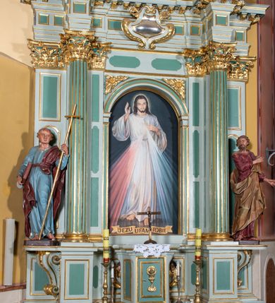 Zdjęcie nr 2: Ołtarz przyścienny, prostopadłościenny, z antepedium, na którym umieszczone są rzeźbione litery IHS; mensa drewniana z kamiennym portatylem. Na mensie znajduje się tabernakulum o kształcie graniastosłupa, z drzwiczkami ozdobionymi rzeźbionym kielichem z hostią. Nastawa ołtarzowa jest architektoniczna, jednoosiowa, jednokondygnacyjna ze zwieńczeniem. Osadzona na podwójnym postumencie, flankowana pilastrami o kompozytowych kapitelach i kanelowanymi kolumnami o kompozytowych kapitelach, które podtrzymują belkowanie. Ponad belkowaniem znajduje się przełamany przyczółek w formie łuku półkolistego, bogato profilowany, ozdobiony ulistnionymi konsolkami i rozetami oraz girlandami z owoców. W partii fryzu kartusz o fantazyjnym wykroju, ujęty wolutami i listkami akantu. Na belkowaniu siedzą po bokach nagie putta, odziane w opaski na biodrach, a pośrodku znajduje się krzyż osadzony na postumencie z liśćmi. Po obu stronach ołtarza na konsolach o krawędziach ozdobionych ornamentem małżowinowym stoją figury trudnych do identyfikacji świętych, być może apostołów. W centralnej części ołtarza wnęka prostokątna, zamknięta łukiem półkolistym. W niej obraz z przedstawieniem „Jezu ufam Tobie”. 