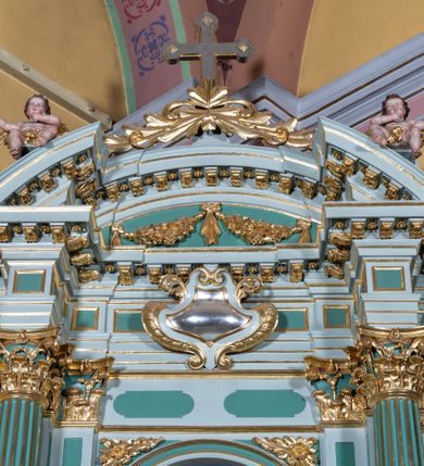 Zdjęcie nr 13: Ołtarz przyścienny, prostopadłościenny, z antepedium, na którym umieszczone są rzeźbione litery IHS; mensa drewniana z kamiennym portatylem. Na mensie znajduje się tabernakulum o kształcie graniastosłupa, z drzwiczkami ozdobionymi rzeźbionym kielichem z hostią. Nastawa ołtarzowa jest architektoniczna, jednoosiowa, jednokondygnacyjna ze zwieńczeniem. Osadzona na podwójnym postumencie, flankowana pilastrami o kompozytowych kapitelach i kanelowanymi kolumnami o kompozytowych kapitelach, które podtrzymują belkowanie. Ponad belkowaniem znajduje się przełamany przyczółek w formie łuku półkolistego, bogato profilowany, ozdobiony ulistnionymi konsolkami i rozetami oraz girlandami z owoców. W partii fryzu kartusz o fantazyjnym wykroju, ujęty wolutami i listkami akantu. Na belkowaniu siedzą po bokach nagie putta, odziane w opaski na biodrach, a pośrodku znajduje się krzyż osadzony na postumencie z liśćmi. Po obu stronach ołtarza na konsolach o krawędziach ozdobionych ornamentem małżowinowym stoją figury trudnych do identyfikacji świętych, być może apostołów. W centralnej części ołtarza wnęka prostokątna, zamknięta łukiem półkolistym. W niej obraz z przedstawieniem „Jezu ufam Tobie”. 