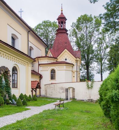 Zdjęcie nr 5: Kompleks klasztorny jest na rzucie czworoboku, z wirydarzem pośrodku i kościołem przylegającym od wschodu. Kościół, zwrócony w kierunku południowo-wschodnim, jest budowlą murowaną z cegły i kamienia, na rzucie podłużnym. Korpus jest jednonawowy i dwuprzęsłowy. Do dwuprzęsłowego prezbiterium na rzucie prostokąta od wschodu przylega zakrystia, do korpusu nawowego kaplica na rzucie ośmioboku z niewysoką przyległością, natomiast do fasady kruchta. Nawa i prezbiterium przekryte są sklepieniami kolebkowymi z lunetami wspartymi na masywnych półfilarach. Przestrzeń prezbiterium od korpusu nawowego oddziela półkolista arkada łuku tęczowego. Artykulację ścian na zewnątrz kościoła stanowią ujmujące okna duże, prostokątne płyciny. Korpus i prezbiterium obiega gzyms koronujący. Szczyt kościoła trójkątny, kruchty w formie nadwieszonego łuku z wycinka elipsy z wklęsłymi uskokami. Do wnętrza prowadzą dwa otwory drzwiowe po wschodniej i północnej stronie kruchty z parą prostokątnych, dwuskrzydłowych drzwi. W szczycie fasady płytka wnęka w kształcie stojącego prostokąta zamkniętego półkoliście z wizerunkiem Niepokalanego Poczęcia Najświętszej Marii Panny, ujęta trzema okrągłymi oknami. W szczycie kruchty analogiczna wnęka z figurą św. Floriana. Pośrodku fasady duże okno w kształcie stojącego prostokąta zamkniętego łukiem odcinkowym. Analogiczne okna w przęsłach korpusu i prezbiterium oraz na jego zamknięciu. Szczyt prezbiterium artykułuje płytka wnęka w kształcie stojącego prostokąta zamkniętego półkoliście z wizerunkiem św. Franciszka adorującego Jezusa na krzyżu flankowana parą okrągłych okien. Korpus i prezbiterium przekryte dachami dwuspadowymi, nad prezbiterium wieżyczka na sygnaturkę. Ściany kaplicy bocznej w formie półkolistych arkad, wypełnionych dużymi oknami z dekoracją maswerkową w górnej partii i przeszklonym otworem drzwiowym, zwieńczonych trójkątnymi szczytami. Ujmują je pary pilastrów, szczyty artykułuje fryz arkadkowy. Kaplicę wieńczy hełm pinaklowy z latarnią. Ściany sąsiedniej przyległości, nakrytej dachem pulpitowym i zakrystii z dachem trójspadowym, artykułuje fryz arkadkowy z lizenami. Tynki pomalowane są w odcieniach żółci. 