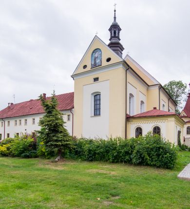 Zdjęcie nr 25: Kompleks klasztorny jest na rzucie czworoboku, z wirydarzem pośrodku i kościołem przylegającym od wschodu. Kościół, zwrócony w kierunku południowo-wschodnim, jest budowlą murowaną z cegły i kamienia, na rzucie podłużnym. Korpus jest jednonawowy i dwuprzęsłowy. Do dwuprzęsłowego prezbiterium na rzucie prostokąta od wschodu przylega zakrystia, do korpusu nawowego kaplica na rzucie ośmioboku z niewysoką przyległością, natomiast do fasady kruchta. Nawa i prezbiterium przekryte są sklepieniami kolebkowymi z lunetami wspartymi na masywnych półfilarach. Przestrzeń prezbiterium od korpusu nawowego oddziela półkolista arkada łuku tęczowego. Artykulację ścian na zewnątrz kościoła stanowią ujmujące okna duże, prostokątne płyciny. Korpus i prezbiterium obiega gzyms koronujący. Szczyt kościoła trójkątny, kruchty w formie nadwieszonego łuku z wycinka elipsy z wklęsłymi uskokami. Do wnętrza prowadzą dwa otwory drzwiowe po wschodniej i północnej stronie kruchty z parą prostokątnych, dwuskrzydłowych drzwi. W szczycie fasady płytka wnęka w kształcie stojącego prostokąta zamkniętego półkoliście z wizerunkiem Niepokalanego Poczęcia Najświętszej Marii Panny, ujęta trzema okrągłymi oknami. W szczycie kruchty analogiczna wnęka z figurą św. Floriana. Pośrodku fasady duże okno w kształcie stojącego prostokąta zamkniętego łukiem odcinkowym. Analogiczne okna w przęsłach korpusu i prezbiterium oraz na jego zamknięciu. Szczyt prezbiterium artykułuje płytka wnęka w kształcie stojącego prostokąta zamkniętego półkoliście z wizerunkiem św. Franciszka adorującego Jezusa na krzyżu flankowana parą okrągłych okien. Korpus i prezbiterium przekryte dachami dwuspadowymi, nad prezbiterium wieżyczka na sygnaturkę. Ściany kaplicy bocznej w formie półkolistych arkad, wypełnionych dużymi oknami z dekoracją maswerkową w górnej partii i przeszklonym otworem drzwiowym, zwieńczonych trójkątnymi szczytami. Ujmują je pary pilastrów, szczyty artykułuje fryz arkadkowy. Kaplicę wieńczy hełm pinaklowy z latarnią. Ściany sąsiedniej przyległości, nakrytej dachem pulpitowym i zakrystii z dachem trójspadowym, artykułuje fryz arkadkowy z lizenami. Tynki pomalowane są w odcieniach żółci. 