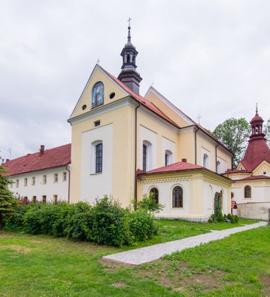 Zdjęcie nr 26: Kompleks klasztorny jest na rzucie czworoboku, z wirydarzem pośrodku i kościołem przylegającym od wschodu. Kościół, zwrócony w kierunku południowo-wschodnim, jest budowlą murowaną z cegły i kamienia, na rzucie podłużnym. Korpus jest jednonawowy i dwuprzęsłowy. Do dwuprzęsłowego prezbiterium na rzucie prostokąta od wschodu przylega zakrystia, do korpusu nawowego kaplica na rzucie ośmioboku z niewysoką przyległością, natomiast do fasady kruchta. Nawa i prezbiterium przekryte są sklepieniami kolebkowymi z lunetami wspartymi na masywnych półfilarach. Przestrzeń prezbiterium od korpusu nawowego oddziela półkolista arkada łuku tęczowego. Artykulację ścian na zewnątrz kościoła stanowią ujmujące okna duże, prostokątne płyciny. Korpus i prezbiterium obiega gzyms koronujący. Szczyt kościoła trójkątny, kruchty w formie nadwieszonego łuku z wycinka elipsy z wklęsłymi uskokami. Do wnętrza prowadzą dwa otwory drzwiowe po wschodniej i północnej stronie kruchty z parą prostokątnych, dwuskrzydłowych drzwi. W szczycie fasady płytka wnęka w kształcie stojącego prostokąta zamkniętego półkoliście z wizerunkiem Niepokalanego Poczęcia Najświętszej Marii Panny, ujęta trzema okrągłymi oknami. W szczycie kruchty analogiczna wnęka z figurą św. Floriana. Pośrodku fasady duże okno w kształcie stojącego prostokąta zamkniętego łukiem odcinkowym. Analogiczne okna w przęsłach korpusu i prezbiterium oraz na jego zamknięciu. Szczyt prezbiterium artykułuje płytka wnęka w kształcie stojącego prostokąta zamkniętego półkoliście z wizerunkiem św. Franciszka adorującego Jezusa na krzyżu flankowana parą okrągłych okien. Korpus i prezbiterium przekryte dachami dwuspadowymi, nad prezbiterium wieżyczka na sygnaturkę. Ściany kaplicy bocznej w formie półkolistych arkad, wypełnionych dużymi oknami z dekoracją maswerkową w górnej partii i przeszklonym otworem drzwiowym, zwieńczonych trójkątnymi szczytami. Ujmują je pary pilastrów, szczyty artykułuje fryz arkadkowy. Kaplicę wieńczy hełm pinaklowy z latarnią. Ściany sąsiedniej przyległości, nakrytej dachem pulpitowym i zakrystii z dachem trójspadowym, artykułuje fryz arkadkowy z lizenami. Tynki pomalowane są w odcieniach żółci. 
