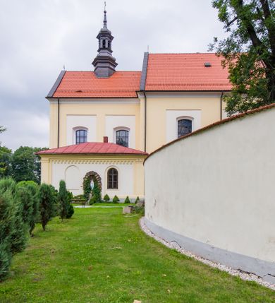 Zdjęcie nr 3: Kompleks klasztorny jest na rzucie czworoboku, z wirydarzem pośrodku i kościołem przylegającym od wschodu. Kościół, zwrócony w kierunku południowo-wschodnim, jest budowlą murowaną z cegły i kamienia, na rzucie podłużnym. Korpus jest jednonawowy i dwuprzęsłowy. Do dwuprzęsłowego prezbiterium na rzucie prostokąta od wschodu przylega zakrystia, do korpusu nawowego kaplica na rzucie ośmioboku z niewysoką przyległością, natomiast do fasady kruchta. Nawa i prezbiterium przekryte są sklepieniami kolebkowymi z lunetami wspartymi na masywnych półfilarach. Przestrzeń prezbiterium od korpusu nawowego oddziela półkolista arkada łuku tęczowego. Artykulację ścian na zewnątrz kościoła stanowią ujmujące okna duże, prostokątne płyciny. Korpus i prezbiterium obiega gzyms koronujący. Szczyt kościoła trójkątny, kruchty w formie nadwieszonego łuku z wycinka elipsy z wklęsłymi uskokami. Do wnętrza prowadzą dwa otwory drzwiowe po wschodniej i północnej stronie kruchty z parą prostokątnych, dwuskrzydłowych drzwi. W szczycie fasady płytka wnęka w kształcie stojącego prostokąta zamkniętego półkoliście z wizerunkiem Niepokalanego Poczęcia Najświętszej Marii Panny, ujęta trzema okrągłymi oknami. W szczycie kruchty analogiczna wnęka z figurą św. Floriana. Pośrodku fasady duże okno w kształcie stojącego prostokąta zamkniętego łukiem odcinkowym. Analogiczne okna w przęsłach korpusu i prezbiterium oraz na jego zamknięciu. Szczyt prezbiterium artykułuje płytka wnęka w kształcie stojącego prostokąta zamkniętego półkoliście z wizerunkiem św. Franciszka adorującego Jezusa na krzyżu flankowana parą okrągłych okien. Korpus i prezbiterium przekryte dachami dwuspadowymi, nad prezbiterium wieżyczka na sygnaturkę. Ściany kaplicy bocznej w formie półkolistych arkad, wypełnionych dużymi oknami z dekoracją maswerkową w górnej partii i przeszklonym otworem drzwiowym, zwieńczonych trójkątnymi szczytami. Ujmują je pary pilastrów, szczyty artykułuje fryz arkadkowy. Kaplicę wieńczy hełm pinaklowy z latarnią. Ściany sąsiedniej przyległości, nakrytej dachem pulpitowym i zakrystii z dachem trójspadowym, artykułuje fryz arkadkowy z lizenami. Tynki pomalowane są w odcieniach żółci. 