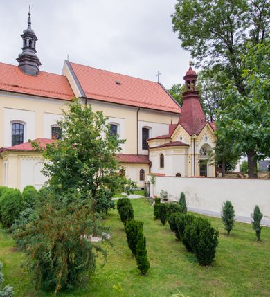Zdjęcie nr 4: Kompleks klasztorny jest na rzucie czworoboku, z wirydarzem pośrodku i kościołem przylegającym od wschodu. Kościół, zwrócony w kierunku południowo-wschodnim, jest budowlą murowaną z cegły i kamienia, na rzucie podłużnym. Korpus jest jednonawowy i dwuprzęsłowy. Do dwuprzęsłowego prezbiterium na rzucie prostokąta od wschodu przylega zakrystia, do korpusu nawowego kaplica na rzucie ośmioboku z niewysoką przyległością, natomiast do fasady kruchta. Nawa i prezbiterium przekryte są sklepieniami kolebkowymi z lunetami wspartymi na masywnych półfilarach. Przestrzeń prezbiterium od korpusu nawowego oddziela półkolista arkada łuku tęczowego. Artykulację ścian na zewnątrz kościoła stanowią ujmujące okna duże, prostokątne płyciny. Korpus i prezbiterium obiega gzyms koronujący. Szczyt kościoła trójkątny, kruchty w formie nadwieszonego łuku z wycinka elipsy z wklęsłymi uskokami. Do wnętrza prowadzą dwa otwory drzwiowe po wschodniej i północnej stronie kruchty z parą prostokątnych, dwuskrzydłowych drzwi. W szczycie fasady płytka wnęka w kształcie stojącego prostokąta zamkniętego półkoliście z wizerunkiem Niepokalanego Poczęcia Najświętszej Marii Panny, ujęta trzema okrągłymi oknami. W szczycie kruchty analogiczna wnęka z figurą św. Floriana. Pośrodku fasady duże okno w kształcie stojącego prostokąta zamkniętego łukiem odcinkowym. Analogiczne okna w przęsłach korpusu i prezbiterium oraz na jego zamknięciu. Szczyt prezbiterium artykułuje płytka wnęka w kształcie stojącego prostokąta zamkniętego półkoliście z wizerunkiem św. Franciszka adorującego Jezusa na krzyżu flankowana parą okrągłych okien. Korpus i prezbiterium przekryte dachami dwuspadowymi, nad prezbiterium wieżyczka na sygnaturkę. Ściany kaplicy bocznej w formie półkolistych arkad, wypełnionych dużymi oknami z dekoracją maswerkową w górnej partii i przeszklonym otworem drzwiowym, zwieńczonych trójkątnymi szczytami. Ujmują je pary pilastrów, szczyty artykułuje fryz arkadkowy. Kaplicę wieńczy hełm pinaklowy z latarnią. Ściany sąsiedniej przyległości, nakrytej dachem pulpitowym i zakrystii z dachem trójspadowym, artykułuje fryz arkadkowy z lizenami. Tynki pomalowane są w odcieniach żółci. 