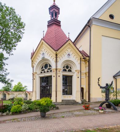 Zdjęcie nr 24: Kompleks klasztorny jest na rzucie czworoboku, z wirydarzem pośrodku i kościołem przylegającym od wschodu. Kościół, zwrócony w kierunku południowo-wschodnim, jest budowlą murowaną z cegły i kamienia, na rzucie podłużnym. Korpus jest jednonawowy i dwuprzęsłowy. Do dwuprzęsłowego prezbiterium na rzucie prostokąta od wschodu przylega zakrystia, do korpusu nawowego kaplica na rzucie ośmioboku z niewysoką przyległością, natomiast do fasady kruchta. Nawa i prezbiterium przekryte są sklepieniami kolebkowymi z lunetami wspartymi na masywnych półfilarach. Przestrzeń prezbiterium od korpusu nawowego oddziela półkolista arkada łuku tęczowego. Artykulację ścian na zewnątrz kościoła stanowią ujmujące okna duże, prostokątne płyciny. Korpus i prezbiterium obiega gzyms koronujący. Szczyt kościoła trójkątny, kruchty w formie nadwieszonego łuku z wycinka elipsy z wklęsłymi uskokami. Do wnętrza prowadzą dwa otwory drzwiowe po wschodniej i północnej stronie kruchty z parą prostokątnych, dwuskrzydłowych drzwi. W szczycie fasady płytka wnęka w kształcie stojącego prostokąta zamkniętego półkoliście z wizerunkiem Niepokalanego Poczęcia Najświętszej Marii Panny, ujęta trzema okrągłymi oknami. W szczycie kruchty analogiczna wnęka z figurą św. Floriana. Pośrodku fasady duże okno w kształcie stojącego prostokąta zamkniętego łukiem odcinkowym. Analogiczne okna w przęsłach korpusu i prezbiterium oraz na jego zamknięciu. Szczyt prezbiterium artykułuje płytka wnęka w kształcie stojącego prostokąta zamkniętego półkoliście z wizerunkiem św. Franciszka adorującego Jezusa na krzyżu flankowana parą okrągłych okien. Korpus i prezbiterium przekryte dachami dwuspadowymi, nad prezbiterium wieżyczka na sygnaturkę. Ściany kaplicy bocznej w formie półkolistych arkad, wypełnionych dużymi oknami z dekoracją maswerkową w górnej partii i przeszklonym otworem drzwiowym, zwieńczonych trójkątnymi szczytami. Ujmują je pary pilastrów, szczyty artykułuje fryz arkadkowy. Kaplicę wieńczy hełm pinaklowy z latarnią. Ściany sąsiedniej przyległości, nakrytej dachem pulpitowym i zakrystii z dachem trójspadowym, artykułuje fryz arkadkowy z lizenami. Tynki pomalowane są w odcieniach żółci. 