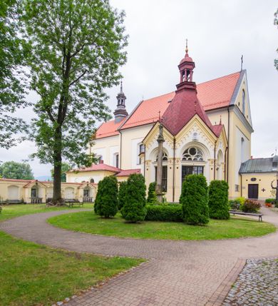 Zdjęcie nr 2: Kompleks klasztorny jest na rzucie czworoboku, z wirydarzem pośrodku i kościołem przylegającym od wschodu. Kościół, zwrócony w kierunku południowo-wschodnim, jest budowlą murowaną z cegły i kamienia, na rzucie podłużnym. Korpus jest jednonawowy i dwuprzęsłowy. Do dwuprzęsłowego prezbiterium na rzucie prostokąta od wschodu przylega zakrystia, do korpusu nawowego kaplica na rzucie ośmioboku z niewysoką przyległością, natomiast do fasady kruchta. Nawa i prezbiterium przekryte są sklepieniami kolebkowymi z lunetami wspartymi na masywnych półfilarach. Przestrzeń prezbiterium od korpusu nawowego oddziela półkolista arkada łuku tęczowego. Artykulację ścian na zewnątrz kościoła stanowią ujmujące okna duże, prostokątne płyciny. Korpus i prezbiterium obiega gzyms koronujący. Szczyt kościoła trójkątny, kruchty w formie nadwieszonego łuku z wycinka elipsy z wklęsłymi uskokami. Do wnętrza prowadzą dwa otwory drzwiowe po wschodniej i północnej stronie kruchty z parą prostokątnych, dwuskrzydłowych drzwi. W szczycie fasady płytka wnęka w kształcie stojącego prostokąta zamkniętego półkoliście z wizerunkiem Niepokalanego Poczęcia Najświętszej Marii Panny, ujęta trzema okrągłymi oknami. W szczycie kruchty analogiczna wnęka z figurą św. Floriana. Pośrodku fasady duże okno w kształcie stojącego prostokąta zamkniętego łukiem odcinkowym. Analogiczne okna w przęsłach korpusu i prezbiterium oraz na jego zamknięciu. Szczyt prezbiterium artykułuje płytka wnęka w kształcie stojącego prostokąta zamkniętego półkoliście z wizerunkiem św. Franciszka adorującego Jezusa na krzyżu flankowana parą okrągłych okien. Korpus i prezbiterium przekryte dachami dwuspadowymi, nad prezbiterium wieżyczka na sygnaturkę. Ściany kaplicy bocznej w formie półkolistych arkad, wypełnionych dużymi oknami z dekoracją maswerkową w górnej partii i przeszklonym otworem drzwiowym, zwieńczonych trójkątnymi szczytami. Ujmują je pary pilastrów, szczyty artykułuje fryz arkadkowy. Kaplicę wieńczy hełm pinaklowy z latarnią. Ściany sąsiedniej przyległości, nakrytej dachem pulpitowym i zakrystii z dachem trójspadowym, artykułuje fryz arkadkowy z lizenami. Tynki pomalowane są w odcieniach żółci. 