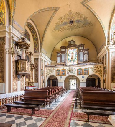 Zdjęcie nr 18: Kompleks klasztorny jest na rzucie czworoboku, z wirydarzem pośrodku i kościołem przylegającym od wschodu. Kościół, zwrócony w kierunku południowo-wschodnim, jest budowlą murowaną z cegły i kamienia, na rzucie podłużnym. Korpus jest jednonawowy i dwuprzęsłowy. Do dwuprzęsłowego prezbiterium na rzucie prostokąta od wschodu przylega zakrystia, do korpusu nawowego kaplica na rzucie ośmioboku z niewysoką przyległością, natomiast do fasady kruchta. Nawa i prezbiterium przekryte są sklepieniami kolebkowymi z lunetami wspartymi na masywnych półfilarach. Przestrzeń prezbiterium od korpusu nawowego oddziela półkolista arkada łuku tęczowego. Artykulację ścian na zewnątrz kościoła stanowią ujmujące okna duże, prostokątne płyciny. Korpus i prezbiterium obiega gzyms koronujący. Szczyt kościoła trójkątny, kruchty w formie nadwieszonego łuku z wycinka elipsy z wklęsłymi uskokami. Do wnętrza prowadzą dwa otwory drzwiowe po wschodniej i północnej stronie kruchty z parą prostokątnych, dwuskrzydłowych drzwi. W szczycie fasady płytka wnęka w kształcie stojącego prostokąta zamkniętego półkoliście z wizerunkiem Niepokalanego Poczęcia Najświętszej Marii Panny, ujęta trzema okrągłymi oknami. W szczycie kruchty analogiczna wnęka z figurą św. Floriana. Pośrodku fasady duże okno w kształcie stojącego prostokąta zamkniętego łukiem odcinkowym. Analogiczne okna w przęsłach korpusu i prezbiterium oraz na jego zamknięciu. Szczyt prezbiterium artykułuje płytka wnęka w kształcie stojącego prostokąta zamkniętego półkoliście z wizerunkiem św. Franciszka adorującego Jezusa na krzyżu flankowana parą okrągłych okien. Korpus i prezbiterium przekryte dachami dwuspadowymi, nad prezbiterium wieżyczka na sygnaturkę. Ściany kaplicy bocznej w formie półkolistych arkad, wypełnionych dużymi oknami z dekoracją maswerkową w górnej partii i przeszklonym otworem drzwiowym, zwieńczonych trójkątnymi szczytami. Ujmują je pary pilastrów, szczyty artykułuje fryz arkadkowy. Kaplicę wieńczy hełm pinaklowy z latarnią. Ściany sąsiedniej przyległości, nakrytej dachem pulpitowym i zakrystii z dachem trójspadowym, artykułuje fryz arkadkowy z lizenami. Tynki pomalowane są w odcieniach żółci. 