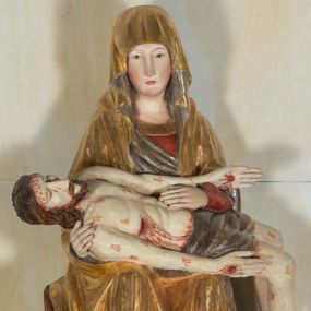 Zdjęcie nr 1: Całopostaciowa, ścięta z tyłu figura przedstawiająca Pietę. Ukazana frontalnie Maria siedzi na prostopadłościennym stołku. Nieznacznie przechyloną w prawo i lekko pochyloną głowę charakteryzują pociągła twarz o owalnym obrysie i subtelnych rysach twarzy, cienkie linie łagodnych łuków brwi, niewielkie oczy o migdałowatym kształcie, długi, prosty nos, drobne usta o lekko opadających kącikach, policzki i podbródek podkreślone rumieńcem. Maria ma na sobie czerwoną suknię z szerokim, złoconym obszyciem dekoltu oraz obszerny, złocony płaszcz o srebrzonym podszyciu, osłaniający głowę, ręce i nogi, o prawej pole podwiniętej pod lewą rękę. Fałdowania przybierają formę drobnych rurek opadających kaskadowo po bokach twarzy oraz w dolnej partii nóg, na wysokości łydek załamujących się w ostre formy w kształcie litery „V”. Maria oburącz podtrzymuje leżące na jej kolanach martwe ciało Jezusa, o zwróconej w lewo sylwetce. Trójkątną twarz charakteryzują wyraziste rysy z niskim czołem, cienką, prostą linią brwi, zamkniętymi oczami, długim, prostym wydatnym nosem, wydatnymi kośćmi policzkowymi, krótkim zarostem. Długie, lekko falowane, brązowe włosy opadają na plecy. Sztywną sylwetkę cechuje także sumarycznie modelowana muskulatura wydatna zwłaszcza w partii brzucha. Długie wyprostowane ręce ułożone są wzdłuż sylwetki, lewa wsparta na lewej ręce Marii; dłonie duże, o wyprostowanych palcach. Długie, zgięte w kolanach nogi o dużych stopach opadają prostopadle do podłoża. Biodra Jezusa przesłania krótkie, ciemnoszare perizonium. Całe ciało o bladej karnacji pokrywają drobne strużki krwi składające się z trzech wydłużonych kropli, na stopach, dłoniach i w prawym boku wydatne, mocno krwawiące rany, czoło wzdłuż linii włosów mocno zakrwawione.  