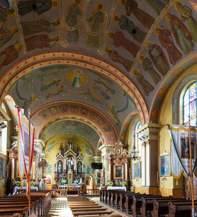 Zdjęcie nr 10: Kościół, zwrócony w kierunku południowo-wschodnim, jest budowlą murowaną z cegły na zaprawie wapiennej, na rzucie podłużnym. Powierzchnia budynku wynosi około 550 m2. Kościół charakteryzuje zwarta, prosta bryła. Korpus jest jednonawowy i trójprzęsłowy. Szerokie, dwuprzęsłowe, prezbiterium jest zamknięte półkoliście. Na osi kościoła, w przedłużeniu północnego przęsła przylega jednokondygnacyjna wieża, ujęta po bokach piętrowymi lokalnościami. Nawa przekryta jest sklepieniem kolebkowym z gurtami, wspartymi na osadzonych na wysokich cokołach parach przyściennych, czworobocznych filarów z przylegającymi do nich pilastrami o gładkich trzonach. Przestrzeń prezbiterium od korpusu nawowego oddziela półkoliście zamknięta arkada łuku tęczowego i drewniana balustrada. Zamknięte prostą ścianą prezbiterium zajmuje przestrzeń jednego przęsła. Dalej znajduje się zakrystia. Artykulację ścian na zewnątrz kościoła stanowi niewysoki obiegający bryłę cokół oraz niepełne belkowanie wieńczące, składające się z fryzu i gzymsu. Fasadę artykułuje płycina podzielona parą wspartych na cokołach pilastrów. W polu środkowym znajduje się główny otwór wejściowy. Dwuskrzydłowe, drewniane drzwi z naświetlem ujęte są prostym, profilowanym portalem. Tuż nad nadprożem znajduje się krótki gzyms. Wyżej duże, prostokątne, zamknięte półkoliście okno. Fasadę wieńczy trójkątny przyczółek. Ściany korpusu nawowego i prezbiterium przeprute są prostokątnymi, zamkniętymi półkoliście oknami. Dodatkowo w ścianie zachodniej, na wysokości przyległości wieży, w dolnej partii muru znajduje się niewielkie, półkoliście zamknięte okno a w drugim przęśle nawy prostokątny otwór drzwiowy; podobny jest umiejscowiony w drugim przęśle prezbiterium po stronie zachodniej. Kondygnację czworobocznej wieży w dolnej partii obiega parapet, wyżej w każdej ze ścian znajduje się po jednym prostokątnym, zamkniętym półkoliście oknie. Górną partię wieży obiega gzyms wieńczący wyłamujący się półkoliście pośrodku każdej ze ścian. Wieża nakryta jest hełmem cebulastym z latarnią. Korpus nawowy i prezbiterium przekrywa dwuspadowy dach wykonany z blachy, z wieżyczką na sygnaturkę na zakończeniu prezbiterium. Kolorystyka tynków kościoła utrzymana jest w odcieniach żółci i bieli, cokół jest brązowy.  Okna nawy, prezbiterium i fasady wypełniają witraże, wnętrze pokrywa polichromia z przedstawieniami figuralnymi w partii sklepień. Plac przykościelny, z wybrukowanymi alejkami i trawnikiem, otoczony jest żywopłotem z krzewów ozdobnych.