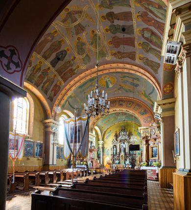 Zdjęcie nr 12: Kościół, zwrócony w kierunku południowo-wschodnim, jest budowlą murowaną z cegły na zaprawie wapiennej, na rzucie podłużnym. Powierzchnia budynku wynosi około 550 m2. Kościół charakteryzuje zwarta, prosta bryła. Korpus jest jednonawowy i trójprzęsłowy. Szerokie, dwuprzęsłowe, prezbiterium jest zamknięte półkoliście. Na osi kościoła, w przedłużeniu północnego przęsła przylega jednokondygnacyjna wieża, ujęta po bokach piętrowymi lokalnościami. Nawa przekryta jest sklepieniem kolebkowym z gurtami, wspartymi na osadzonych na wysokich cokołach parach przyściennych, czworobocznych filarów z przylegającymi do nich pilastrami o gładkich trzonach. Przestrzeń prezbiterium od korpusu nawowego oddziela półkoliście zamknięta arkada łuku tęczowego i drewniana balustrada. Zamknięte prostą ścianą prezbiterium zajmuje przestrzeń jednego przęsła. Dalej znajduje się zakrystia. Artykulację ścian na zewnątrz kościoła stanowi niewysoki obiegający bryłę cokół oraz niepełne belkowanie wieńczące, składające się z fryzu i gzymsu. Fasadę artykułuje płycina podzielona parą wspartych na cokołach pilastrów. W polu środkowym znajduje się główny otwór wejściowy. Dwuskrzydłowe, drewniane drzwi z naświetlem ujęte są prostym, profilowanym portalem. Tuż nad nadprożem znajduje się krótki gzyms. Wyżej duże, prostokątne, zamknięte półkoliście okno. Fasadę wieńczy trójkątny przyczółek. Ściany korpusu nawowego i prezbiterium przeprute są prostokątnymi, zamkniętymi półkoliście oknami. Dodatkowo w ścianie zachodniej, na wysokości przyległości wieży, w dolnej partii muru znajduje się niewielkie, półkoliście zamknięte okno a w drugim przęśle nawy prostokątny otwór drzwiowy; podobny jest umiejscowiony w drugim przęśle prezbiterium po stronie zachodniej. Kondygnację czworobocznej wieży w dolnej partii obiega parapet, wyżej w każdej ze ścian znajduje się po jednym prostokątnym, zamkniętym półkoliście oknie. Górną partię wieży obiega gzyms wieńczący wyłamujący się półkoliście pośrodku każdej ze ścian. Wieża nakryta jest hełmem cebulastym z latarnią. Korpus nawowy i prezbiterium przekrywa dwuspadowy dach wykonany z blachy, z wieżyczką na sygnaturkę na zakończeniu prezbiterium. Kolorystyka tynków kościoła utrzymana jest w odcieniach żółci i bieli, cokół jest brązowy.  Okna nawy, prezbiterium i fasady wypełniają witraże, wnętrze pokrywa polichromia z przedstawieniami figuralnymi w partii sklepień. Plac przykościelny, z wybrukowanymi alejkami i trawnikiem, otoczony jest żywopłotem z krzewów ozdobnych.