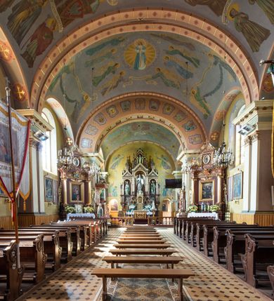 Zdjęcie nr 11: Kościół, zwrócony w kierunku południowo-wschodnim, jest budowlą murowaną z cegły na zaprawie wapiennej, na rzucie podłużnym. Powierzchnia budynku wynosi około 550 m2. Kościół charakteryzuje zwarta, prosta bryła. Korpus jest jednonawowy i trójprzęsłowy. Szerokie, dwuprzęsłowe, prezbiterium jest zamknięte półkoliście. Na osi kościoła, w przedłużeniu północnego przęsła przylega jednokondygnacyjna wieża, ujęta po bokach piętrowymi lokalnościami. Nawa przekryta jest sklepieniem kolebkowym z gurtami, wspartymi na osadzonych na wysokich cokołach parach przyściennych, czworobocznych filarów z przylegającymi do nich pilastrami o gładkich trzonach. Przestrzeń prezbiterium od korpusu nawowego oddziela półkoliście zamknięta arkada łuku tęczowego i drewniana balustrada. Zamknięte prostą ścianą prezbiterium zajmuje przestrzeń jednego przęsła. Dalej znajduje się zakrystia. Artykulację ścian na zewnątrz kościoła stanowi niewysoki obiegający bryłę cokół oraz niepełne belkowanie wieńczące, składające się z fryzu i gzymsu. Fasadę artykułuje płycina podzielona parą wspartych na cokołach pilastrów. W polu środkowym znajduje się główny otwór wejściowy. Dwuskrzydłowe, drewniane drzwi z naświetlem ujęte są prostym, profilowanym portalem. Tuż nad nadprożem znajduje się krótki gzyms. Wyżej duże, prostokątne, zamknięte półkoliście okno. Fasadę wieńczy trójkątny przyczółek. Ściany korpusu nawowego i prezbiterium przeprute są prostokątnymi, zamkniętymi półkoliście oknami. Dodatkowo w ścianie zachodniej, na wysokości przyległości wieży, w dolnej partii muru znajduje się niewielkie, półkoliście zamknięte okno a w drugim przęśle nawy prostokątny otwór drzwiowy; podobny jest umiejscowiony w drugim przęśle prezbiterium po stronie zachodniej. Kondygnację czworobocznej wieży w dolnej partii obiega parapet, wyżej w każdej ze ścian znajduje się po jednym prostokątnym, zamkniętym półkoliście oknie. Górną partię wieży obiega gzyms wieńczący wyłamujący się półkoliście pośrodku każdej ze ścian. Wieża nakryta jest hełmem cebulastym z latarnią. Korpus nawowy i prezbiterium przekrywa dwuspadowy dach wykonany z blachy, z wieżyczką na sygnaturkę na zakończeniu prezbiterium. Kolorystyka tynków kościoła utrzymana jest w odcieniach żółci i bieli, cokół jest brązowy.  Okna nawy, prezbiterium i fasady wypełniają witraże, wnętrze pokrywa polichromia z przedstawieniami figuralnymi w partii sklepień. Plac przykościelny, z wybrukowanymi alejkami i trawnikiem, otoczony jest żywopłotem z krzewów ozdobnych.