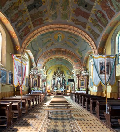 Zdjęcie nr 8: Kościół, zwrócony w kierunku południowo-wschodnim, jest budowlą murowaną z cegły na zaprawie wapiennej, na rzucie podłużnym. Powierzchnia budynku wynosi około 550 m2. Kościół charakteryzuje zwarta, prosta bryła. Korpus jest jednonawowy i trójprzęsłowy. Szerokie, dwuprzęsłowe, prezbiterium jest zamknięte półkoliście. Na osi kościoła, w przedłużeniu północnego przęsła przylega jednokondygnacyjna wieża, ujęta po bokach piętrowymi lokalnościami. Nawa przekryta jest sklepieniem kolebkowym z gurtami, wspartymi na osadzonych na wysokich cokołach parach przyściennych, czworobocznych filarów z przylegającymi do nich pilastrami o gładkich trzonach. Przestrzeń prezbiterium od korpusu nawowego oddziela półkoliście zamknięta arkada łuku tęczowego i drewniana balustrada. Zamknięte prostą ścianą prezbiterium zajmuje przestrzeń jednego przęsła. Dalej znajduje się zakrystia. Artykulację ścian na zewnątrz kościoła stanowi niewysoki obiegający bryłę cokół oraz niepełne belkowanie wieńczące, składające się z fryzu i gzymsu. Fasadę artykułuje płycina podzielona parą wspartych na cokołach pilastrów. W polu środkowym znajduje się główny otwór wejściowy. Dwuskrzydłowe, drewniane drzwi z naświetlem ujęte są prostym, profilowanym portalem. Tuż nad nadprożem znajduje się krótki gzyms. Wyżej duże, prostokątne, zamknięte półkoliście okno. Fasadę wieńczy trójkątny przyczółek. Ściany korpusu nawowego i prezbiterium przeprute są prostokątnymi, zamkniętymi półkoliście oknami. Dodatkowo w ścianie zachodniej, na wysokości przyległości wieży, w dolnej partii muru znajduje się niewielkie, półkoliście zamknięte okno a w drugim przęśle nawy prostokątny otwór drzwiowy; podobny jest umiejscowiony w drugim przęśle prezbiterium po stronie zachodniej. Kondygnację czworobocznej wieży w dolnej partii obiega parapet, wyżej w każdej ze ścian znajduje się po jednym prostokątnym, zamkniętym półkoliście oknie. Górną partię wieży obiega gzyms wieńczący wyłamujący się półkoliście pośrodku każdej ze ścian. Wieża nakryta jest hełmem cebulastym z latarnią. Korpus nawowy i prezbiterium przekrywa dwuspadowy dach wykonany z blachy, z wieżyczką na sygnaturkę na zakończeniu prezbiterium. Kolorystyka tynków kościoła utrzymana jest w odcieniach żółci i bieli, cokół jest brązowy.  Okna nawy, prezbiterium i fasady wypełniają witraże, wnętrze pokrywa polichromia z przedstawieniami figuralnymi w partii sklepień. Plac przykościelny, z wybrukowanymi alejkami i trawnikiem, otoczony jest żywopłotem z krzewów ozdobnych.