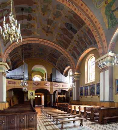 Zdjęcie nr 14: Kościół, zwrócony w kierunku południowo-wschodnim, jest budowlą murowaną z cegły na zaprawie wapiennej, na rzucie podłużnym. Powierzchnia budynku wynosi około 550 m2. Kościół charakteryzuje zwarta, prosta bryła. Korpus jest jednonawowy i trójprzęsłowy. Szerokie, dwuprzęsłowe, prezbiterium jest zamknięte półkoliście. Na osi kościoła, w przedłużeniu północnego przęsła przylega jednokondygnacyjna wieża, ujęta po bokach piętrowymi lokalnościami. Nawa przekryta jest sklepieniem kolebkowym z gurtami, wspartymi na osadzonych na wysokich cokołach parach przyściennych, czworobocznych filarów z przylegającymi do nich pilastrami o gładkich trzonach. Przestrzeń prezbiterium od korpusu nawowego oddziela półkoliście zamknięta arkada łuku tęczowego i drewniana balustrada. Zamknięte prostą ścianą prezbiterium zajmuje przestrzeń jednego przęsła. Dalej znajduje się zakrystia. Artykulację ścian na zewnątrz kościoła stanowi niewysoki obiegający bryłę cokół oraz niepełne belkowanie wieńczące, składające się z fryzu i gzymsu. Fasadę artykułuje płycina podzielona parą wspartych na cokołach pilastrów. W polu środkowym znajduje się główny otwór wejściowy. Dwuskrzydłowe, drewniane drzwi z naświetlem ujęte są prostym, profilowanym portalem. Tuż nad nadprożem znajduje się krótki gzyms. Wyżej duże, prostokątne, zamknięte półkoliście okno. Fasadę wieńczy trójkątny przyczółek. Ściany korpusu nawowego i prezbiterium przeprute są prostokątnymi, zamkniętymi półkoliście oknami. Dodatkowo w ścianie zachodniej, na wysokości przyległości wieży, w dolnej partii muru znajduje się niewielkie, półkoliście zamknięte okno a w drugim przęśle nawy prostokątny otwór drzwiowy; podobny jest umiejscowiony w drugim przęśle prezbiterium po stronie zachodniej. Kondygnację czworobocznej wieży w dolnej partii obiega parapet, wyżej w każdej ze ścian znajduje się po jednym prostokątnym, zamkniętym półkoliście oknie. Górną partię wieży obiega gzyms wieńczący wyłamujący się półkoliście pośrodku każdej ze ścian. Wieża nakryta jest hełmem cebulastym z latarnią. Korpus nawowy i prezbiterium przekrywa dwuspadowy dach wykonany z blachy, z wieżyczką na sygnaturkę na zakończeniu prezbiterium. Kolorystyka tynków kościoła utrzymana jest w odcieniach żółci i bieli, cokół jest brązowy.  Okna nawy, prezbiterium i fasady wypełniają witraże, wnętrze pokrywa polichromia z przedstawieniami figuralnymi w partii sklepień. Plac przykościelny, z wybrukowanymi alejkami i trawnikiem, otoczony jest żywopłotem z krzewów ozdobnych.