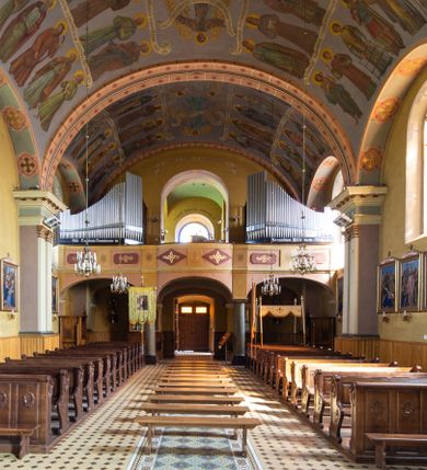 Zdjęcie nr 16: Kościół, zwrócony w kierunku południowo-wschodnim, jest budowlą murowaną z cegły na zaprawie wapiennej, na rzucie podłużnym. Powierzchnia budynku wynosi około 550 m2. Kościół charakteryzuje zwarta, prosta bryła. Korpus jest jednonawowy i trójprzęsłowy. Szerokie, dwuprzęsłowe, prezbiterium jest zamknięte półkoliście. Na osi kościoła, w przedłużeniu północnego przęsła przylega jednokondygnacyjna wieża, ujęta po bokach piętrowymi lokalnościami. Nawa przekryta jest sklepieniem kolebkowym z gurtami, wspartymi na osadzonych na wysokich cokołach parach przyściennych, czworobocznych filarów z przylegającymi do nich pilastrami o gładkich trzonach. Przestrzeń prezbiterium od korpusu nawowego oddziela półkoliście zamknięta arkada łuku tęczowego i drewniana balustrada. Zamknięte prostą ścianą prezbiterium zajmuje przestrzeń jednego przęsła. Dalej znajduje się zakrystia. Artykulację ścian na zewnątrz kościoła stanowi niewysoki obiegający bryłę cokół oraz niepełne belkowanie wieńczące, składające się z fryzu i gzymsu. Fasadę artykułuje płycina podzielona parą wspartych na cokołach pilastrów. W polu środkowym znajduje się główny otwór wejściowy. Dwuskrzydłowe, drewniane drzwi z naświetlem ujęte są prostym, profilowanym portalem. Tuż nad nadprożem znajduje się krótki gzyms. Wyżej duże, prostokątne, zamknięte półkoliście okno. Fasadę wieńczy trójkątny przyczółek. Ściany korpusu nawowego i prezbiterium przeprute są prostokątnymi, zamkniętymi półkoliście oknami. Dodatkowo w ścianie zachodniej, na wysokości przyległości wieży, w dolnej partii muru znajduje się niewielkie, półkoliście zamknięte okno a w drugim przęśle nawy prostokątny otwór drzwiowy; podobny jest umiejscowiony w drugim przęśle prezbiterium po stronie zachodniej. Kondygnację czworobocznej wieży w dolnej partii obiega parapet, wyżej w każdej ze ścian znajduje się po jednym prostokątnym, zamkniętym półkoliście oknie. Górną partię wieży obiega gzyms wieńczący wyłamujący się półkoliście pośrodku każdej ze ścian. Wieża nakryta jest hełmem cebulastym z latarnią. Korpus nawowy i prezbiterium przekrywa dwuspadowy dach wykonany z blachy, z wieżyczką na sygnaturkę na zakończeniu prezbiterium. Kolorystyka tynków kościoła utrzymana jest w odcieniach żółci i bieli, cokół jest brązowy.  Okna nawy, prezbiterium i fasady wypełniają witraże, wnętrze pokrywa polichromia z przedstawieniami figuralnymi w partii sklepień. Plac przykościelny, z wybrukowanymi alejkami i trawnikiem, otoczony jest żywopłotem z krzewów ozdobnych.