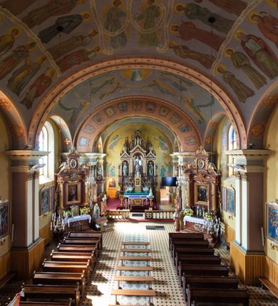 Zdjęcie nr 7: Kościół, zwrócony w kierunku południowo-wschodnim, jest budowlą murowaną z cegły na zaprawie wapiennej, na rzucie podłużnym. Powierzchnia budynku wynosi około 550 m2. Kościół charakteryzuje zwarta, prosta bryła. Korpus jest jednonawowy i trójprzęsłowy. Szerokie, dwuprzęsłowe, prezbiterium jest zamknięte półkoliście. Na osi kościoła, w przedłużeniu północnego przęsła przylega jednokondygnacyjna wieża, ujęta po bokach piętrowymi lokalnościami. Nawa przekryta jest sklepieniem kolebkowym z gurtami, wspartymi na osadzonych na wysokich cokołach parach przyściennych, czworobocznych filarów z przylegającymi do nich pilastrami o gładkich trzonach. Przestrzeń prezbiterium od korpusu nawowego oddziela półkoliście zamknięta arkada łuku tęczowego i drewniana balustrada. Zamknięte prostą ścianą prezbiterium zajmuje przestrzeń jednego przęsła. Dalej znajduje się zakrystia. Artykulację ścian na zewnątrz kościoła stanowi niewysoki obiegający bryłę cokół oraz niepełne belkowanie wieńczące, składające się z fryzu i gzymsu. Fasadę artykułuje płycina podzielona parą wspartych na cokołach pilastrów. W polu środkowym znajduje się główny otwór wejściowy. Dwuskrzydłowe, drewniane drzwi z naświetlem ujęte są prostym, profilowanym portalem. Tuż nad nadprożem znajduje się krótki gzyms. Wyżej duże, prostokątne, zamknięte półkoliście okno. Fasadę wieńczy trójkątny przyczółek. Ściany korpusu nawowego i prezbiterium przeprute są prostokątnymi, zamkniętymi półkoliście oknami. Dodatkowo w ścianie zachodniej, na wysokości przyległości wieży, w dolnej partii muru znajduje się niewielkie, półkoliście zamknięte okno a w drugim przęśle nawy prostokątny otwór drzwiowy; podobny jest umiejscowiony w drugim przęśle prezbiterium po stronie zachodniej. Kondygnację czworobocznej wieży w dolnej partii obiega parapet, wyżej w każdej ze ścian znajduje się po jednym prostokątnym, zamkniętym półkoliście oknie. Górną partię wieży obiega gzyms wieńczący wyłamujący się półkoliście pośrodku każdej ze ścian. Wieża nakryta jest hełmem cebulastym z latarnią. Korpus nawowy i prezbiterium przekrywa dwuspadowy dach wykonany z blachy, z wieżyczką na sygnaturkę na zakończeniu prezbiterium. Kolorystyka tynków kościoła utrzymana jest w odcieniach żółci i bieli, cokół jest brązowy.  Okna nawy, prezbiterium i fasady wypełniają witraże, wnętrze pokrywa polichromia z przedstawieniami figuralnymi w partii sklepień. Plac przykościelny, z wybrukowanymi alejkami i trawnikiem, otoczony jest żywopłotem z krzewów ozdobnych.