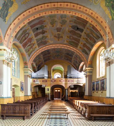 Zdjęcie nr 15: Kościół, zwrócony w kierunku południowo-wschodnim, jest budowlą murowaną z cegły na zaprawie wapiennej, na rzucie podłużnym. Powierzchnia budynku wynosi około 550 m2. Kościół charakteryzuje zwarta, prosta bryła. Korpus jest jednonawowy i trójprzęsłowy. Szerokie, dwuprzęsłowe, prezbiterium jest zamknięte półkoliście. Na osi kościoła, w przedłużeniu północnego przęsła przylega jednokondygnacyjna wieża, ujęta po bokach piętrowymi lokalnościami. Nawa przekryta jest sklepieniem kolebkowym z gurtami, wspartymi na osadzonych na wysokich cokołach parach przyściennych, czworobocznych filarów z przylegającymi do nich pilastrami o gładkich trzonach. Przestrzeń prezbiterium od korpusu nawowego oddziela półkoliście zamknięta arkada łuku tęczowego i drewniana balustrada. Zamknięte prostą ścianą prezbiterium zajmuje przestrzeń jednego przęsła. Dalej znajduje się zakrystia. Artykulację ścian na zewnątrz kościoła stanowi niewysoki obiegający bryłę cokół oraz niepełne belkowanie wieńczące, składające się z fryzu i gzymsu. Fasadę artykułuje płycina podzielona parą wspartych na cokołach pilastrów. W polu środkowym znajduje się główny otwór wejściowy. Dwuskrzydłowe, drewniane drzwi z naświetlem ujęte są prostym, profilowanym portalem. Tuż nad nadprożem znajduje się krótki gzyms. Wyżej duże, prostokątne, zamknięte półkoliście okno. Fasadę wieńczy trójkątny przyczółek. Ściany korpusu nawowego i prezbiterium przeprute są prostokątnymi, zamkniętymi półkoliście oknami. Dodatkowo w ścianie zachodniej, na wysokości przyległości wieży, w dolnej partii muru znajduje się niewielkie, półkoliście zamknięte okno a w drugim przęśle nawy prostokątny otwór drzwiowy; podobny jest umiejscowiony w drugim przęśle prezbiterium po stronie zachodniej. Kondygnację czworobocznej wieży w dolnej partii obiega parapet, wyżej w każdej ze ścian znajduje się po jednym prostokątnym, zamkniętym półkoliście oknie. Górną partię wieży obiega gzyms wieńczący wyłamujący się półkoliście pośrodku każdej ze ścian. Wieża nakryta jest hełmem cebulastym z latarnią. Korpus nawowy i prezbiterium przekrywa dwuspadowy dach wykonany z blachy, z wieżyczką na sygnaturkę na zakończeniu prezbiterium. Kolorystyka tynków kościoła utrzymana jest w odcieniach żółci i bieli, cokół jest brązowy.  Okna nawy, prezbiterium i fasady wypełniają witraże, wnętrze pokrywa polichromia z przedstawieniami figuralnymi w partii sklepień. Plac przykościelny, z wybrukowanymi alejkami i trawnikiem, otoczony jest żywopłotem z krzewów ozdobnych.