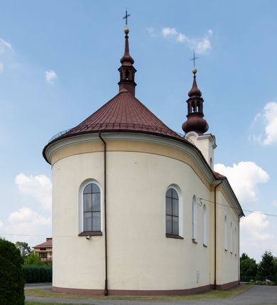 Zdjęcie nr 4: Kościół, zwrócony w kierunku południowo-wschodnim, jest budowlą murowaną z cegły na zaprawie wapiennej, na rzucie podłużnym. Powierzchnia budynku wynosi około 550 m2. Kościół charakteryzuje zwarta, prosta bryła. Korpus jest jednonawowy i trójprzęsłowy. Szerokie, dwuprzęsłowe, prezbiterium jest zamknięte półkoliście. Na osi kościoła, w przedłużeniu północnego przęsła przylega jednokondygnacyjna wieża, ujęta po bokach piętrowymi lokalnościami. Nawa przekryta jest sklepieniem kolebkowym z gurtami, wspartymi na osadzonych na wysokich cokołach parach przyściennych, czworobocznych filarów z przylegającymi do nich pilastrami o gładkich trzonach. Przestrzeń prezbiterium od korpusu nawowego oddziela półkoliście zamknięta arkada łuku tęczowego i drewniana balustrada. Zamknięte prostą ścianą prezbiterium zajmuje przestrzeń jednego przęsła. Dalej znajduje się zakrystia. Artykulację ścian na zewnątrz kościoła stanowi niewysoki obiegający bryłę cokół oraz niepełne belkowanie wieńczące, składające się z fryzu i gzymsu. Fasadę artykułuje płycina podzielona parą wspartych na cokołach pilastrów. W polu środkowym znajduje się główny otwór wejściowy. Dwuskrzydłowe, drewniane drzwi z naświetlem ujęte są prostym, profilowanym portalem. Tuż nad nadprożem znajduje się krótki gzyms. Wyżej duże, prostokątne, zamknięte półkoliście okno. Fasadę wieńczy trójkątny przyczółek. Ściany korpusu nawowego i prezbiterium przeprute są prostokątnymi, zamkniętymi półkoliście oknami. Dodatkowo w ścianie zachodniej, na wysokości przyległości wieży, w dolnej partii muru znajduje się niewielkie, półkoliście zamknięte okno a w drugim przęśle nawy prostokątny otwór drzwiowy; podobny jest umiejscowiony w drugim przęśle prezbiterium po stronie zachodniej. Kondygnację czworobocznej wieży w dolnej partii obiega parapet, wyżej w każdej ze ścian znajduje się po jednym prostokątnym, zamkniętym półkoliście oknie. Górną partię wieży obiega gzyms wieńczący wyłamujący się półkoliście pośrodku każdej ze ścian. Wieża nakryta jest hełmem cebulastym z latarnią. Korpus nawowy i prezbiterium przekrywa dwuspadowy dach wykonany z blachy, z wieżyczką na sygnaturkę na zakończeniu prezbiterium. Kolorystyka tynków kościoła utrzymana jest w odcieniach żółci i bieli, cokół jest brązowy.  Okna nawy, prezbiterium i fasady wypełniają witraże, wnętrze pokrywa polichromia z przedstawieniami figuralnymi w partii sklepień. Plac przykościelny, z wybrukowanymi alejkami i trawnikiem, otoczony jest żywopłotem z krzewów ozdobnych.