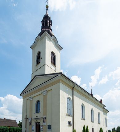 Zdjęcie nr 2: Kościół, zwrócony w kierunku południowo-wschodnim, jest budowlą murowaną z cegły na zaprawie wapiennej, na rzucie podłużnym. Powierzchnia budynku wynosi około 550 m2. Kościół charakteryzuje zwarta, prosta bryła. Korpus jest jednonawowy i trójprzęsłowy. Szerokie, dwuprzęsłowe, prezbiterium jest zamknięte półkoliście. Na osi kościoła, w przedłużeniu północnego przęsła przylega jednokondygnacyjna wieża, ujęta po bokach piętrowymi lokalnościami. Nawa przekryta jest sklepieniem kolebkowym z gurtami, wspartymi na osadzonych na wysokich cokołach parach przyściennych, czworobocznych filarów z przylegającymi do nich pilastrami o gładkich trzonach. Przestrzeń prezbiterium od korpusu nawowego oddziela półkoliście zamknięta arkada łuku tęczowego i drewniana balustrada. Zamknięte prostą ścianą prezbiterium zajmuje przestrzeń jednego przęsła. Dalej znajduje się zakrystia. Artykulację ścian na zewnątrz kościoła stanowi niewysoki obiegający bryłę cokół oraz niepełne belkowanie wieńczące, składające się z fryzu i gzymsu. Fasadę artykułuje płycina podzielona parą wspartych na cokołach pilastrów. W polu środkowym znajduje się główny otwór wejściowy. Dwuskrzydłowe, drewniane drzwi z naświetlem ujęte są prostym, profilowanym portalem. Tuż nad nadprożem znajduje się krótki gzyms. Wyżej duże, prostokątne, zamknięte półkoliście okno. Fasadę wieńczy trójkątny przyczółek. Ściany korpusu nawowego i prezbiterium przeprute są prostokątnymi, zamkniętymi półkoliście oknami. Dodatkowo w ścianie zachodniej, na wysokości przyległości wieży, w dolnej partii muru znajduje się niewielkie, półkoliście zamknięte okno a w drugim przęśle nawy prostokątny otwór drzwiowy; podobny jest umiejscowiony w drugim przęśle prezbiterium po stronie zachodniej. Kondygnację czworobocznej wieży w dolnej partii obiega parapet, wyżej w każdej ze ścian znajduje się po jednym prostokątnym, zamkniętym półkoliście oknie. Górną partię wieży obiega gzyms wieńczący wyłamujący się półkoliście pośrodku każdej ze ścian. Wieża nakryta jest hełmem cebulastym z latarnią. Korpus nawowy i prezbiterium przekrywa dwuspadowy dach wykonany z blachy, z wieżyczką na sygnaturkę na zakończeniu prezbiterium. Kolorystyka tynków kościoła utrzymana jest w odcieniach żółci i bieli, cokół jest brązowy.  Okna nawy, prezbiterium i fasady wypełniają witraże, wnętrze pokrywa polichromia z przedstawieniami figuralnymi w partii sklepień. Plac przykościelny, z wybrukowanymi alejkami i trawnikiem, otoczony jest żywopłotem z krzewów ozdobnych.
