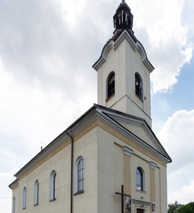 Zdjęcie nr 3: Kościół, zwrócony w kierunku południowo-wschodnim, jest budowlą murowaną z cegły na zaprawie wapiennej, na rzucie podłużnym. Powierzchnia budynku wynosi około 550 m2. Kościół charakteryzuje zwarta, prosta bryła. Korpus jest jednonawowy i trójprzęsłowy. Szerokie, dwuprzęsłowe, prezbiterium jest zamknięte półkoliście. Na osi kościoła, w przedłużeniu północnego przęsła przylega jednokondygnacyjna wieża, ujęta po bokach piętrowymi lokalnościami. Nawa przekryta jest sklepieniem kolebkowym z gurtami, wspartymi na osadzonych na wysokich cokołach parach przyściennych, czworobocznych filarów z przylegającymi do nich pilastrami o gładkich trzonach. Przestrzeń prezbiterium od korpusu nawowego oddziela półkoliście zamknięta arkada łuku tęczowego i drewniana balustrada. Zamknięte prostą ścianą prezbiterium zajmuje przestrzeń jednego przęsła. Dalej znajduje się zakrystia. Artykulację ścian na zewnątrz kościoła stanowi niewysoki obiegający bryłę cokół oraz niepełne belkowanie wieńczące, składające się z fryzu i gzymsu. Fasadę artykułuje płycina podzielona parą wspartych na cokołach pilastrów. W polu środkowym znajduje się główny otwór wejściowy. Dwuskrzydłowe, drewniane drzwi z naświetlem ujęte są prostym, profilowanym portalem. Tuż nad nadprożem znajduje się krótki gzyms. Wyżej duże, prostokątne, zamknięte półkoliście okno. Fasadę wieńczy trójkątny przyczółek. Ściany korpusu nawowego i prezbiterium przeprute są prostokątnymi, zamkniętymi półkoliście oknami. Dodatkowo w ścianie zachodniej, na wysokości przyległości wieży, w dolnej partii muru znajduje się niewielkie, półkoliście zamknięte okno a w drugim przęśle nawy prostokątny otwór drzwiowy; podobny jest umiejscowiony w drugim przęśle prezbiterium po stronie zachodniej. Kondygnację czworobocznej wieży w dolnej partii obiega parapet, wyżej w każdej ze ścian znajduje się po jednym prostokątnym, zamkniętym półkoliście oknie. Górną partię wieży obiega gzyms wieńczący wyłamujący się półkoliście pośrodku każdej ze ścian. Wieża nakryta jest hełmem cebulastym z latarnią. Korpus nawowy i prezbiterium przekrywa dwuspadowy dach wykonany z blachy, z wieżyczką na sygnaturkę na zakończeniu prezbiterium. Kolorystyka tynków kościoła utrzymana jest w odcieniach żółci i bieli, cokół jest brązowy.  Okna nawy, prezbiterium i fasady wypełniają witraże, wnętrze pokrywa polichromia z przedstawieniami figuralnymi w partii sklepień. Plac przykościelny, z wybrukowanymi alejkami i trawnikiem, otoczony jest żywopłotem z krzewów ozdobnych.