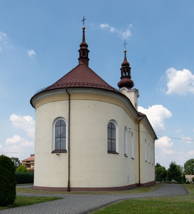 Zdjęcie nr 5: Kościół, zwrócony w kierunku południowo-wschodnim, jest budowlą murowaną z cegły na zaprawie wapiennej, na rzucie podłużnym. Powierzchnia budynku wynosi około 550 m2. Kościół charakteryzuje zwarta, prosta bryła. Korpus jest jednonawowy i trójprzęsłowy. Szerokie, dwuprzęsłowe, prezbiterium jest zamknięte półkoliście. Na osi kościoła, w przedłużeniu północnego przęsła przylega jednokondygnacyjna wieża, ujęta po bokach piętrowymi lokalnościami. Nawa przekryta jest sklepieniem kolebkowym z gurtami, wspartymi na osadzonych na wysokich cokołach parach przyściennych, czworobocznych filarów z przylegającymi do nich pilastrami o gładkich trzonach. Przestrzeń prezbiterium od korpusu nawowego oddziela półkoliście zamknięta arkada łuku tęczowego i drewniana balustrada. Zamknięte prostą ścianą prezbiterium zajmuje przestrzeń jednego przęsła. Dalej znajduje się zakrystia. Artykulację ścian na zewnątrz kościoła stanowi niewysoki obiegający bryłę cokół oraz niepełne belkowanie wieńczące, składające się z fryzu i gzymsu. Fasadę artykułuje płycina podzielona parą wspartych na cokołach pilastrów. W polu środkowym znajduje się główny otwór wejściowy. Dwuskrzydłowe, drewniane drzwi z naświetlem ujęte są prostym, profilowanym portalem. Tuż nad nadprożem znajduje się krótki gzyms. Wyżej duże, prostokątne, zamknięte półkoliście okno. Fasadę wieńczy trójkątny przyczółek. Ściany korpusu nawowego i prezbiterium przeprute są prostokątnymi, zamkniętymi półkoliście oknami. Dodatkowo w ścianie zachodniej, na wysokości przyległości wieży, w dolnej partii muru znajduje się niewielkie, półkoliście zamknięte okno a w drugim przęśle nawy prostokątny otwór drzwiowy; podobny jest umiejscowiony w drugim przęśle prezbiterium po stronie zachodniej. Kondygnację czworobocznej wieży w dolnej partii obiega parapet, wyżej w każdej ze ścian znajduje się po jednym prostokątnym, zamkniętym półkoliście oknie. Górną partię wieży obiega gzyms wieńczący wyłamujący się półkoliście pośrodku każdej ze ścian. Wieża nakryta jest hełmem cebulastym z latarnią. Korpus nawowy i prezbiterium przekrywa dwuspadowy dach wykonany z blachy, z wieżyczką na sygnaturkę na zakończeniu prezbiterium. Kolorystyka tynków kościoła utrzymana jest w odcieniach żółci i bieli, cokół jest brązowy.  Okna nawy, prezbiterium i fasady wypełniają witraże, wnętrze pokrywa polichromia z przedstawieniami figuralnymi w partii sklepień. Plac przykościelny, z wybrukowanymi alejkami i trawnikiem, otoczony jest żywopłotem z krzewów ozdobnych.