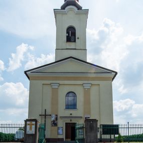 Zdjęcie nr 1: Kościół, zwrócony w kierunku południowo-wschodnim, jest budowlą murowaną z cegły na zaprawie wapiennej, na rzucie podłużnym. Powierzchnia budynku wynosi około 550 m2. Kościół charakteryzuje zwarta, prosta bryła. Korpus jest jednonawowy i trójprzęsłowy. Szerokie, dwuprzęsłowe, prezbiterium jest zamknięte półkoliście. Na osi kościoła, w przedłużeniu północnego przęsła przylega jednokondygnacyjna wieża, ujęta po bokach piętrowymi lokalnościami. Nawa przekryta jest sklepieniem kolebkowym z gurtami, wspartymi na osadzonych na wysokich cokołach parach przyściennych, czworobocznych filarów z przylegającymi do nich pilastrami o gładkich trzonach. Przestrzeń prezbiterium od korpusu nawowego oddziela półkoliście zamknięta arkada łuku tęczowego i drewniana balustrada. Zamknięte prostą ścianą prezbiterium zajmuje przestrzeń jednego przęsła. Dalej znajduje się zakrystia. Artykulację ścian na zewnątrz kościoła stanowi niewysoki obiegający bryłę cokół oraz niepełne belkowanie wieńczące, składające się z fryzu i gzymsu. Fasadę artykułuje płycina podzielona parą wspartych na cokołach pilastrów. W polu środkowym znajduje się główny otwór wejściowy. Dwuskrzydłowe, drewniane drzwi z naświetlem ujęte są prostym, profilowanym portalem. Tuż nad nadprożem znajduje się krótki gzyms. Wyżej duże, prostokątne, zamknięte półkoliście okno. Fasadę wieńczy trójkątny przyczółek. Ściany korpusu nawowego i prezbiterium przeprute są prostokątnymi, zamkniętymi półkoliście oknami. Dodatkowo w ścianie zachodniej, na wysokości przyległości wieży, w dolnej partii muru znajduje się niewielkie, półkoliście zamknięte okno a w drugim przęśle nawy prostokątny otwór drzwiowy; podobny jest umiejscowiony w drugim przęśle prezbiterium po stronie zachodniej. Kondygnację czworobocznej wieży w dolnej partii obiega parapet, wyżej w każdej ze ścian znajduje się po jednym prostokątnym, zamkniętym półkoliście oknie. Górną partię wieży obiega gzyms wieńczący wyłamujący się półkoliście pośrodku każdej ze ścian. Wieża nakryta jest hełmem cebulastym z latarnią. Korpus nawowy i prezbiterium przekrywa dwuspadowy dach wykonany z blachy, z wieżyczką na sygnaturkę na zakończeniu prezbiterium. Kolorystyka tynków kościoła utrzymana jest w odcieniach żółci i bieli, cokół jest brązowy.  Okna nawy, prezbiterium i fasady wypełniają witraże, wnętrze pokrywa polichromia z przedstawieniami figuralnymi w partii sklepień. Plac przykościelny, z wybrukowanymi alejkami i trawnikiem, otoczony jest żywopłotem z krzewów ozdobnych.