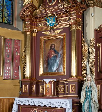 Zdjęcie nr 2: Ołtarz architektoniczny, jednoosiowy, jednokondygnacyjny, ze zwieńczeniem. Retabulum osadzone jest na wysokim, zdwojonym, zryzalitowanym uskokowo cokole. Ołtarz jest prostopadłościenny z drewnianą mensą. Pośrodku mensy znajduje się tabernakulum w formie prostopadłościennej szafki o lekko wypukłej przedniej ściance. Z przodu naroża ujmuje para półkolumienek, z tyłu półwałków. Prostokątne, zamknięte łukiem wklęsło-wypukłym drzwiczki zdobi polichromowane przedstawienie kielicha eucharystycznego na obłokach. Część środkową retabulum ujmuje para kolumn o żłobkowanych trzonach i korynckich kapitelach, ustawionych na tle zdwojonych pilastrów. Podpory dźwigają wyłamujące się ponad nimi belkowanie o silnie wysuniętym gzymsie. Zwieńczenie ma formę aediculi ujętej parą pilastrów i spływów wolutowych, zamkniętej trójkątnym przyczółkiem. Dodatkowo ujęta jest ona przerwanym, półkolistym przyczółkiem. Płycina antepedium jest w kształcie leżącego prostokąta z płaskorzeźbionym motywem złoconego, gorejącego serca, krzyża i kotwicy na tle srebrzonych obłoków ujętych promienistą glorią. Płyciny górnego cokołu (predelli) wypełnia stylizowana ornamentyka roślinna. Część środkową ujmuje para ażurowych uszaków z motywem kwiatu oraz wici akantu. U góry, pośrodku znajduje się uskrzydlona główka anielska. Powyżej, w partii belkowania, którego gzyms zdobi kostokowanie, umieszczony jest kartusz herbowy z monogramem maryjnym. Fryz zdobi stylizowana wić roślinna oraz para uskrzydlonych główek anielskich, natomiast zwieńczenie retabulum m.in. motywy roślinne, rozetki i kampanule. Szczyt tworzy podtrzymująca koronę para aniołów o sylwetkach od pasa w dół w formie liści akantu. Na przerwanym przyczółku znajduje się para przysiadających aniołów w sukniach w kolorze jasnofioletowym i pomarańczowym oraz złoconych płaszczach. Pole w części środkowej ma kształt stojącego prostokąta ujętego profilowaną, złoconą ramą. W środku znajduje się wizerunek Najświętszego Serca Jezusa. Pole w zwieńczeniu ma kształt stojącego owalu ujętego złoconą ramą w formie wieńca laurowego. Zawiera scenę Chrztu Jezusa w Jordanie. 
Struktura retabulum utrzymana jest w odcieniach brązu, partie detalu architektonicznego i ornamentyka są złocone. 
