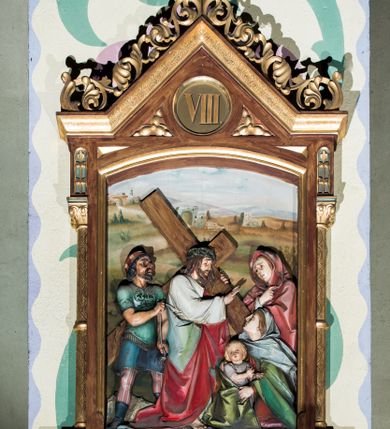 Zdjęcie nr 8: Czternaście płaskorzeźbionych stacji Drogi krzyżowej składa się z przedstawienia ujętego w taką samą architektoniczną, drewnianą ramę. Pole obrazowe uzyskał kształt stojącego prostokąta zamkniętego u góry łukiem odcinkowym. Flankują go smukłe półkolumienki wsparte na niskich bazach, ustawionych na prostokątnym, profilowanym cokole wspartym od dołu po bokach niewielkimi konsolami oraz udekorowanym podwieszonym na osi stylizowanym ornamentem roślinnym. Na cokole umieszczono podpis poszczególnej stacji. Kolumienki podtrzymują profilowane belkowanie w kształcie nadwieszonego trójkąta zwieńczonego krzyżem. Zewnętrze boki trójkąta zdobi ażurowy, złocony ornament roślinny. W polu trójkąta w medalionie wpisano kolejny numer stacji. Strukturę obramienia polichromowano na brązowo, natomiast kolumienki, wieńczące krzyże, ornamenty oraz profile zostały pozłocone. W polach obrazowych znalazły się wielopostaciowe, płaskorzeźbione kompozycje umieszczone najczęściej na tle pejzażu i architektury. Narracja każdego z obrazów skupia się na osobie Chrystusa, któremu towarzyszą inni ludzie, zgodnie z narracją kolejnej stacji. Przedstawione postacie wykonują gwałtowne i dynamiczne gesty. Na ich twarzach o jasnych karnacjach widoczne są różne emocje. Postacie ubrane są w obficie drapowane szaty o intensywnej i kontrastowej kolorystyce. Cykl przedstawia stacje z następującymi podpisami: I. Pan Jezus przez Piłata na śmierć skazany, II. Pan Jezus bierze krzyż na barki, III. Pan Jezus upada po raz pierwszy, IV. Pan Jezus spotyka się ze swoją Matką, V. Panu Jezusowi dopomaga Szymon Cyrenejczyk, VI. Panu Jezusowi ociera twarz św. Weronika, VII. Pan Jezus upada drugi raz, VIII. Pan Jezus pociesza płaczące niewiasty, IX. Pan Jezus upada po raz trzeci, X. Pan Jezus obnażony i żółcią napawany, XI. Pan Jezus do krzyża przybijany, XII. Pan Jezus umiera na krzyżu, XIII. Pan Jezus z krzyża zdjęty, XIV. Pan Jezus złożony w grobie. 