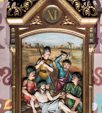 Zdjęcie nr 11: Czternaście płaskorzeźbionych stacji Drogi krzyżowej składa się z przedstawienia ujętego w taką samą architektoniczną, drewnianą ramę. Pole obrazowe uzyskał kształt stojącego prostokąta zamkniętego u góry łukiem odcinkowym. Flankują go smukłe półkolumienki wsparte na niskich bazach, ustawionych na prostokątnym, profilowanym cokole wspartym od dołu po bokach niewielkimi konsolami oraz udekorowanym podwieszonym na osi stylizowanym ornamentem roślinnym. Na cokole umieszczono podpis poszczególnej stacji. Kolumienki podtrzymują profilowane belkowanie w kształcie nadwieszonego trójkąta zwieńczonego krzyżem. Zewnętrze boki trójkąta zdobi ażurowy, złocony ornament roślinny. W polu trójkąta w medalionie wpisano kolejny numer stacji. Strukturę obramienia polichromowano na brązowo, natomiast kolumienki, wieńczące krzyże, ornamenty oraz profile zostały pozłocone. W polach obrazowych znalazły się wielopostaciowe, płaskorzeźbione kompozycje umieszczone najczęściej na tle pejzażu i architektury. Narracja każdego z obrazów skupia się na osobie Chrystusa, któremu towarzyszą inni ludzie, zgodnie z narracją kolejnej stacji. Przedstawione postacie wykonują gwałtowne i dynamiczne gesty. Na ich twarzach o jasnych karnacjach widoczne są różne emocje. Postacie ubrane są w obficie drapowane szaty o intensywnej i kontrastowej kolorystyce. Cykl przedstawia stacje z następującymi podpisami: I. Pan Jezus przez Piłata na śmierć skazany, II. Pan Jezus bierze krzyż na barki, III. Pan Jezus upada po raz pierwszy, IV. Pan Jezus spotyka się ze swoją Matką, V. Panu Jezusowi dopomaga Szymon Cyrenejczyk, VI. Panu Jezusowi ociera twarz św. Weronika, VII. Pan Jezus upada drugi raz, VIII. Pan Jezus pociesza płaczące niewiasty, IX. Pan Jezus upada po raz trzeci, X. Pan Jezus obnażony i żółcią napawany, XI. Pan Jezus do krzyża przybijany, XII. Pan Jezus umiera na krzyżu, XIII. Pan Jezus z krzyża zdjęty, XIV. Pan Jezus złożony w grobie. 