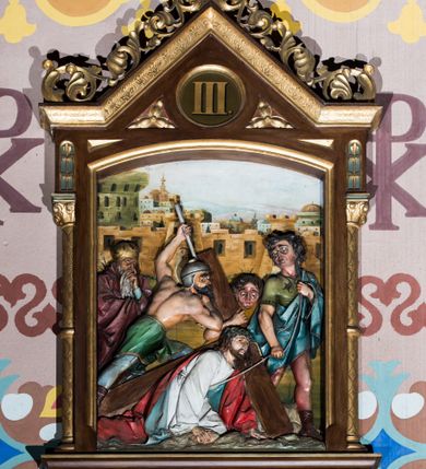 Zdjęcie nr 3: Czternaście płaskorzeźbionych stacji Drogi krzyżowej składa się z przedstawienia ujętego w taką samą architektoniczną, drewnianą ramę. Pole obrazowe uzyskał kształt stojącego prostokąta zamkniętego u góry łukiem odcinkowym. Flankują go smukłe półkolumienki wsparte na niskich bazach, ustawionych na prostokątnym, profilowanym cokole wspartym od dołu po bokach niewielkimi konsolami oraz udekorowanym podwieszonym na osi stylizowanym ornamentem roślinnym. Na cokole umieszczono podpis poszczególnej stacji. Kolumienki podtrzymują profilowane belkowanie w kształcie nadwieszonego trójkąta zwieńczonego krzyżem. Zewnętrze boki trójkąta zdobi ażurowy, złocony ornament roślinny. W polu trójkąta w medalionie wpisano kolejny numer stacji. Strukturę obramienia polichromowano na brązowo, natomiast kolumienki, wieńczące krzyże, ornamenty oraz profile zostały pozłocone. W polach obrazowych znalazły się wielopostaciowe, płaskorzeźbione kompozycje umieszczone najczęściej na tle pejzażu i architektury. Narracja każdego z obrazów skupia się na osobie Chrystusa, któremu towarzyszą inni ludzie, zgodnie z narracją kolejnej stacji. Przedstawione postacie wykonują gwałtowne i dynamiczne gesty. Na ich twarzach o jasnych karnacjach widoczne są różne emocje. Postacie ubrane są w obficie drapowane szaty o intensywnej i kontrastowej kolorystyce. Cykl przedstawia stacje z następującymi podpisami: I. Pan Jezus przez Piłata na śmierć skazany, II. Pan Jezus bierze krzyż na barki, III. Pan Jezus upada po raz pierwszy, IV. Pan Jezus spotyka się ze swoją Matką, V. Panu Jezusowi dopomaga Szymon Cyrenejczyk, VI. Panu Jezusowi ociera twarz św. Weronika, VII. Pan Jezus upada drugi raz, VIII. Pan Jezus pociesza płaczące niewiasty, IX. Pan Jezus upada po raz trzeci, X. Pan Jezus obnażony i żółcią napawany, XI. Pan Jezus do krzyża przybijany, XII. Pan Jezus umiera na krzyżu, XIII. Pan Jezus z krzyża zdjęty, XIV. Pan Jezus złożony w grobie. 