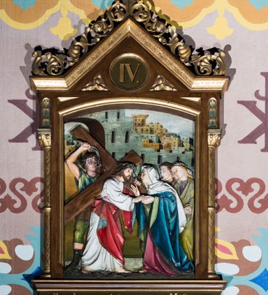 Zdjęcie nr 4: Czternaście płaskorzeźbionych stacji Drogi krzyżowej składa się z przedstawienia ujętego w taką samą architektoniczną, drewnianą ramę. Pole obrazowe uzyskał kształt stojącego prostokąta zamkniętego u góry łukiem odcinkowym. Flankują go smukłe półkolumienki wsparte na niskich bazach, ustawionych na prostokątnym, profilowanym cokole wspartym od dołu po bokach niewielkimi konsolami oraz udekorowanym podwieszonym na osi stylizowanym ornamentem roślinnym. Na cokole umieszczono podpis poszczególnej stacji. Kolumienki podtrzymują profilowane belkowanie w kształcie nadwieszonego trójkąta zwieńczonego krzyżem. Zewnętrze boki trójkąta zdobi ażurowy, złocony ornament roślinny. W polu trójkąta w medalionie wpisano kolejny numer stacji. Strukturę obramienia polichromowano na brązowo, natomiast kolumienki, wieńczące krzyże, ornamenty oraz profile zostały pozłocone. W polach obrazowych znalazły się wielopostaciowe, płaskorzeźbione kompozycje umieszczone najczęściej na tle pejzażu i architektury. Narracja każdego z obrazów skupia się na osobie Chrystusa, któremu towarzyszą inni ludzie, zgodnie z narracją kolejnej stacji. Przedstawione postacie wykonują gwałtowne i dynamiczne gesty. Na ich twarzach o jasnych karnacjach widoczne są różne emocje. Postacie ubrane są w obficie drapowane szaty o intensywnej i kontrastowej kolorystyce. Cykl przedstawia stacje z następującymi podpisami: I. Pan Jezus przez Piłata na śmierć skazany, II. Pan Jezus bierze krzyż na barki, III. Pan Jezus upada po raz pierwszy, IV. Pan Jezus spotyka się ze swoją Matką, V. Panu Jezusowi dopomaga Szymon Cyrenejczyk, VI. Panu Jezusowi ociera twarz św. Weronika, VII. Pan Jezus upada drugi raz, VIII. Pan Jezus pociesza płaczące niewiasty, IX. Pan Jezus upada po raz trzeci, X. Pan Jezus obnażony i żółcią napawany, XI. Pan Jezus do krzyża przybijany, XII. Pan Jezus umiera na krzyżu, XIII. Pan Jezus z krzyża zdjęty, XIV. Pan Jezus złożony w grobie. 