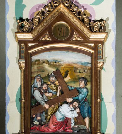 Zdjęcie nr 7: Czternaście płaskorzeźbionych stacji Drogi krzyżowej składa się z przedstawienia ujętego w taką samą architektoniczną, drewnianą ramę. Pole obrazowe uzyskał kształt stojącego prostokąta zamkniętego u góry łukiem odcinkowym. Flankują go smukłe półkolumienki wsparte na niskich bazach, ustawionych na prostokątnym, profilowanym cokole wspartym od dołu po bokach niewielkimi konsolami oraz udekorowanym podwieszonym na osi stylizowanym ornamentem roślinnym. Na cokole umieszczono podpis poszczególnej stacji. Kolumienki podtrzymują profilowane belkowanie w kształcie nadwieszonego trójkąta zwieńczonego krzyżem. Zewnętrze boki trójkąta zdobi ażurowy, złocony ornament roślinny. W polu trójkąta w medalionie wpisano kolejny numer stacji. Strukturę obramienia polichromowano na brązowo, natomiast kolumienki, wieńczące krzyże, ornamenty oraz profile zostały pozłocone. W polach obrazowych znalazły się wielopostaciowe, płaskorzeźbione kompozycje umieszczone najczęściej na tle pejzażu i architektury. Narracja każdego z obrazów skupia się na osobie Chrystusa, któremu towarzyszą inni ludzie, zgodnie z narracją kolejnej stacji. Przedstawione postacie wykonują gwałtowne i dynamiczne gesty. Na ich twarzach o jasnych karnacjach widoczne są różne emocje. Postacie ubrane są w obficie drapowane szaty o intensywnej i kontrastowej kolorystyce. Cykl przedstawia stacje z następującymi podpisami: I. Pan Jezus przez Piłata na śmierć skazany, II. Pan Jezus bierze krzyż na barki, III. Pan Jezus upada po raz pierwszy, IV. Pan Jezus spotyka się ze swoją Matką, V. Panu Jezusowi dopomaga Szymon Cyrenejczyk, VI. Panu Jezusowi ociera twarz św. Weronika, VII. Pan Jezus upada drugi raz, VIII. Pan Jezus pociesza płaczące niewiasty, IX. Pan Jezus upada po raz trzeci, X. Pan Jezus obnażony i żółcią napawany, XI. Pan Jezus do krzyża przybijany, XII. Pan Jezus umiera na krzyżu, XIII. Pan Jezus z krzyża zdjęty, XIV. Pan Jezus złożony w grobie. 