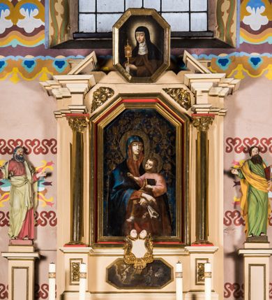 Zdjęcie nr 1: Nastawa ołtarzowa uzyskała charakter przyściennego retabulum jednoosiowego, jednokondygnacyjnego ze zwieńczeniem. Drewniany stipes ołtarzowy przyjął kształt zwężającego się ku dołowi sarkofagu ustawionego na podeście o dwu stopniach, wspierającego mensę. Na mensie na osi ustawiono prostopadłościenne tabernakulum ujęte po bokach spływami wolutowym podtrzymującymi belkowanie. Drzwiczki do tabernakulum uzyskały kształt stojącego prostokąta zamkniętego u góry łukiem nadwieszonym z uskokiem. Retabulum ustawiono na wysokim cokole flankowanym dwoma, dwustrefowymi, przyściennymi filarami, na których ustawiono figury św. Józefa i św. Joachima. Kondygnację nastawy ujmują dwie smukłe kolumny z kapitelami korynckimi, wsparte na dwustopniowych postumentach ustawionych na prostopadłościennych wysuniętych do przodu fragmentach dolnego cokołu, pomiędzy którymi ustawiono tabernakulum. Górną część postumentów zdobią prostokątne płyciny z płaskorzeźbionym ornamentem w polu. Pomiędzy postumentami w strukturze ołtarza umieszczono pole obrazowe w kształcie leżącego prostokąta o ściętych narożach, w którym przedstawiono Zwiastowanie Najświętszej Marii Pannie. Fragment środkowej części tego obrazu przykrywa kartusz zwieńczony dwoma uskrzydlonymi główkami aniołków, a od dołu zakończony muszlą. Kartusz zachodzi także na pole środkowe, które uzyskało kształt prostokąta, zakończonego trójbocznie. Wewnątrz umieszczono w profilowanej ramie obraz Matki Boskiej z Dzieciątkiem w rzymskim typie Salus Populi Romani. Kolumny podtrzymują niepełne, wyłamane na ich osi belkowanie z dwoma przerwanymi przyczółkami. Pomiędzy przyczółkami jako zwieńczenie umieszczono prostokątny obraz o ściętych narożach z przedstawieniem św. Klary. Strukturę ołtarza pomalowano w tonacji jasnobeżowej. Kolumny, profile oraz ornamenty zostały wyzłocone.