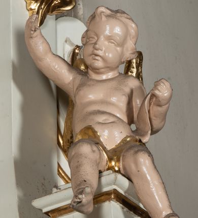 Zdjęcie nr 6: Ołtarz uzyskał formę architektonicznej struktury przyściennej, jednoosiowej, jednokondygnacyjnej ze zwieńczeniem. Marmurowy stipes ołtarzowy z mensą wykonano w formie prostopadłościanu dostawionego do wysokiego podwyższenia z marmuru ustawionego na podeście o ściętych narożach. Lico stipesu zdobi ryty symbol maryjny w otoku otoczonym przez stylizowane ramiona krzyża równoramiennego. Na podwyższeniu wsparto drewnianą strukturę nastawy ustawioną na cokole i flankowaną przez dwa filary. Przed lico kondygnacji wysunięto do przodu dwa postumenty, mające w pierwotnym zamyśle stanowić podpory dla flankujących strukturę dwóch kolumn podtrzymujący belkowanie wyłamane na ich osiach. Z kolumn zrezygnowano, a w ich miejsce w strukturę ołtarza oraz w trzony filarów zewnętrznych wprowadzono podłużne gabloty na wota. W polu kondygnacji wprowadzono prostokątną niszę zamkniętą półkoliście z mniejszym, czworobocznym obrazem Matki Boskiej Nieustającej Pomocy wiszącym na tle z szkarłatnej tkaniny. Poniżej obrazu umieszczono podłużną gablotę na wota. Ramę pola tworzą dwa pilastry o akantowych głowicach i trzonach dekorowanych zawieszonymi na taśmach bukiecikami kwiatów oraz półokrągły łuk, na którym umieszczono główki aniołków ze skrzyżowanymi skrzydełkami. Zwieńczenie utworzono z prostokątnego pola zamkniętego półkoliście ujętego obramieniem artykułowanym za pomocą rzędu kasetonów z rozetami, flankowanego przez dwa pilastry. W polu na niebieskim tle z tkaniny umieszczono ponad girlandą kwiatową w kształcie półksiężyca monogram maryjny także utworzony z girland roślino-kwiatowych. Zwieńczenie ujmuje para spływów wolutowych. Dwa pozostałe spływy wysunięte nad przedpolu zwieńczenia do przodu stanowią podstawę dla pary uskrzydlonych aniołków. Całość zwieńczenia zamyka kartusz prezentowany przez dwa aniołki oraz fantazyjny ornament spływający po jego bokach. W polu kartusza umieszczono napis: "O MARYJO / NIEUSTANNIE / WSPOMAGAJ / NAS". Struktura ołtarza polichromowana w kolorze kości słoniowej, profile i ornamenty zostały wyzłocone.  
