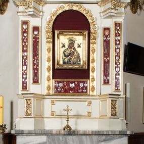 Zdjęcie nr 1: Ołtarz uzyskał formę architektonicznej struktury przyściennej, jednoosiowej, jednokondygnacyjnej ze zwieńczeniem. Marmurowy stipes ołtarzowy z mensą wykonano w formie prostopadłościanu dostawionego do wysokiego podwyższenia z marmuru ustawionego na podeście o ściętych narożach. Lico stipesu zdobi ryty symbol maryjny w otoku otoczonym przez stylizowane ramiona krzyża równoramiennego. Na podwyższeniu wsparto drewnianą strukturę nastawy ustawioną na cokole i flankowaną przez dwa filary. Przed lico kondygnacji wysunięto do przodu dwa postumenty, mające w pierwotnym zamyśle stanowić podpory dla flankujących strukturę dwóch kolumn podtrzymujący belkowanie wyłamane na ich osiach. Z kolumn zrezygnowano, a w ich miejsce w strukturę ołtarza oraz w trzony filarów zewnętrznych wprowadzono podłużne gabloty na wota. W polu kondygnacji wprowadzono prostokątną niszę zamkniętą półkoliście z mniejszym, czworobocznym obrazem Matki Boskiej Nieustającej Pomocy wiszącym na tle z szkarłatnej tkaniny. Poniżej obrazu umieszczono podłużną gablotę na wota. Ramę pola tworzą dwa pilastry o akantowych głowicach i trzonach dekorowanych zawieszonymi na taśmach bukiecikami kwiatów oraz półokrągły łuk, na którym umieszczono główki aniołków ze skrzyżowanymi skrzydełkami. Zwieńczenie utworzono z prostokątnego pola zamkniętego półkoliście ujętego obramieniem artykułowanym za pomocą rzędu kasetonów z rozetami, flankowanego przez dwa pilastry. W polu na niebieskim tle z tkaniny umieszczono ponad girlandą kwiatową w kształcie półksiężyca monogram maryjny także utworzony z girland roślino-kwiatowych. Zwieńczenie ujmuje para spływów wolutowych. Dwa pozostałe spływy wysunięte nad przedpolu zwieńczenia do przodu stanowią podstawę dla pary uskrzydlonych aniołków. Całość zwieńczenia zamyka kartusz prezentowany przez dwa aniołki oraz fantazyjny ornament spływający po jego bokach. W polu kartusza umieszczono napis: "O MARYJO / NIEUSTANNIE / WSPOMAGAJ / NAS". Struktura ołtarza polichromowana w kolorze kości słoniowej, profile i ornamenty zostały wyzłocone.  