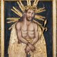 Zdjęcie nr 1: Obraz uzyskał kształt stojącego prostokąta ujętego złoconą, profilowaną ramą z dekoracją w typie wolich oczu. W centrum kompozycji ukazano na ciemnym tle frontalnie w dwóch trzecich Chrystusa z nieznacznie pochyloną głową w lewo ujętą w trzech czwartych. Zbawiciel ma skrzyżowane z przodu i związane sznurem ręce. W lewej dłoni trzyma wygiętą trzcinę. Jezus ma pociągłą twarz o jasnej karnacji okoloną krótką brodą i brązowymi włosami spływającymi na ramiona. Zbawiciel ma duży, prosty nos, wydatne usta i szeroko otwarte ciemne oczy. Na głowie ma złoconą koronę cierniową, spod której spływają krople krwi. Jego głowę otaczają ostre, złocone promienie. Krew widoczna jest także na odsłoniętym torsie oraz rękach. Zbawiciel ubrany jest w płaszcz narzucony na wątłe ramiona odsłaniający jego nagi tors. Zarówno płaszcz, jak i korona cierniowa, trzcina oraz sznur zostały przykryte płaskorzeźbioną, drewnianą sukienką wotywną. 