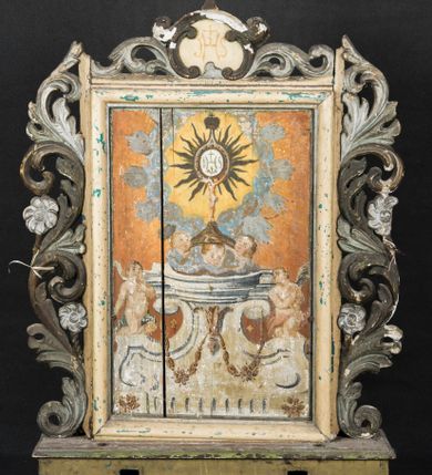 Zdjęcie nr 1: Feretron utworzono z prostopadłościennej podstawy w formie wydłużonego postumentu z otworami przeznaczonymi na drążki do noszenia oraz czworobocznego obramienia dekorowanego z trzech stron pierwotnie złoconą, ażurową wicią stylizowanego akantu z kwiatami. Na zwieńczeniu w owalu wyobrażona na awersie monogram maryjny a na rewersie chrystogram "IHS". Dwustronne pole obrazowe uzyskało kształt stojącego prostokąta. Na rewersie w pole feretronu wpisano prostokątną, profilowaną ramą zakończoną u góry nadwieszonym łukiem odcinkowym z uskokiem, którą flankują dwa grzebienie rocaillowe. W polu ramy ukazano Trójcę Przenajświętszą. Frontalnie ujęty Bóg Ojciec został wyobrażony z prawej strony kompozycji jako siwobrody starzec o bujnych siwych włosach. W prawej ręce trzyma złote berło, lewą zaś odsuwa od siebie. Jego obie stopy opierają się na umieszczonym po środku globie ziemskim. Twarz Boga Ojca charakteryzuje jasna karnacja, szeroko otwarte oczy, wydatny nos i usta. Obok Boga Ojca z lewej strony siedzi Chrystus, który obie nogi wspiera na globie. Zbawiciel trzymający oburącz drewniany krzyż oparty o swoje lewe ramię został przedstawiony w trzech czwartych w prawo. Jest to dojrzały mężczyzna o pociągłej twarzy okolonej brązowymi, długimi włosami spływającymi na ramiona oraz krótką brodą. Ma jasną karnację, prosty nos i wydatne usta. Nagi tors okrywa w partii bioder rozwiany, bladoszkarłatny płaszcz odsłaniający prawą stopę. Na dłoniach i stopach widoczne są rany po gwoździach. Głowę Jezusa otacza świetlisty nimb. Powyżej obu postaci unosi się gołębica Ducha Świętego w promienistym otoku. Obraz na rewersie został ujęty profilowaną, prostokątną ramą. W centrum kompozycji na ochrowym tle na architektonicznym tronie wystawienia, utworzonym z odcinka wklęsłego belkowania wspartego na dwóch spływach wolutowych, przechodzących w dwa flankujące go cokoły ukazano wspartą na trzech uskrzydlonych główkach anielskich promienistą monstrancję z hostią. Monstrancja zwieńczona zamkniętą koroną została namalowana na jaśniejącym tle otoczonym obłokami z promieniami. W jej centrum na hostii umieszczono chrystogram "IHS". Po bokach tronu na cokołach klęczą dwa nagie uskrzydlone aniołki.  