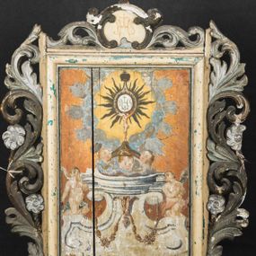 Zdjęcie nr 1: Feretron utworzono z prostopadłościennej podstawy w formie wydłużonego postumentu z otworami przeznaczonymi na drążki do noszenia oraz czworobocznego obramienia dekorowanego z trzech stron pierwotnie złoconą, ażurową wicią stylizowanego akantu z kwiatami. Na zwieńczeniu w owalu wyobrażona na awersie monogram maryjny a na rewersie chrystogram "IHS". Dwustronne pole obrazowe uzyskało kształt stojącego prostokąta. Na rewersie w pole feretronu wpisano prostokątną, profilowaną ramą zakończoną u góry nadwieszonym łukiem odcinkowym z uskokiem, którą flankują dwa grzebienie rocaillowe. W polu ramy ukazano Trójcę Przenajświętszą. Frontalnie ujęty Bóg Ojciec został wyobrażony z prawej strony kompozycji jako siwobrody starzec o bujnych siwych włosach. W prawej ręce trzyma złote berło, lewą zaś odsuwa od siebie. Jego obie stopy opierają się na umieszczonym po środku globie ziemskim. Twarz Boga Ojca charakteryzuje jasna karnacja, szeroko otwarte oczy, wydatny nos i usta. Obok Boga Ojca z lewej strony siedzi Chrystus, który obie nogi wspiera na globie. Zbawiciel trzymający oburącz drewniany krzyż oparty o swoje lewe ramię został przedstawiony w trzech czwartych w prawo. Jest to dojrzały mężczyzna o pociągłej twarzy okolonej brązowymi, długimi włosami spływającymi na ramiona oraz krótką brodą. Ma jasną karnację, prosty nos i wydatne usta. Nagi tors okrywa w partii bioder rozwiany, bladoszkarłatny płaszcz odsłaniający prawą stopę. Na dłoniach i stopach widoczne są rany po gwoździach. Głowę Jezusa otacza świetlisty nimb. Powyżej obu postaci unosi się gołębica Ducha Świętego w promienistym otoku. Obraz na rewersie został ujęty profilowaną, prostokątną ramą. W centrum kompozycji na ochrowym tle na architektonicznym tronie wystawienia, utworzonym z odcinka wklęsłego belkowania wspartego na dwóch spływach wolutowych, przechodzących w dwa flankujące go cokoły ukazano wspartą na trzech uskrzydlonych główkach anielskich promienistą monstrancję z hostią. Monstrancja zwieńczona zamkniętą koroną została namalowana na jaśniejącym tle otoczonym obłokami z promieniami. W jej centrum na hostii umieszczono chrystogram "IHS". Po bokach tronu na cokołach klęczą dwa nagie uskrzydlone aniołki.  