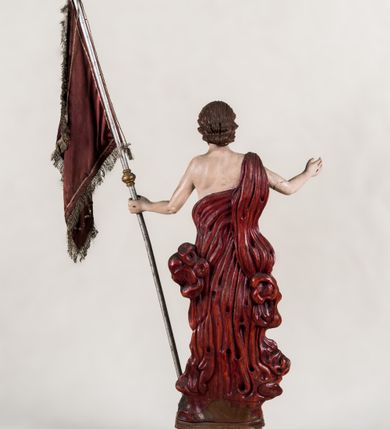 Zdjęcie nr 3: Pełnoplastyczna, całopostaciowa figura ukazuje Chrystusa Zmartwychwstałego stojącego na podłożu imitującym niewielki pagórek, osadzonym na profilowanej, prostopadłościennej podstawie o ściętych narożach. Zbawiciel na lekko ugiętych nogach ukazany został frontalnie. Obie ręce ma uniesione i odsunięte od tułowia. W lewej trzyma chorągiew na drzewcu z czerwonej tkaniny obszytej srebrną frędzlą i dekorowanej cekinami. Z kolei prawa jest uniesiona na wysokości klatki piersiowej. Jego sylwetka została opracowana sumarycznie z próbą uchwycenia muskulatury oraz zaznaczeniem partii żeber. Biodra Zbawiciela okrywa przewiązane, pozłocone perizonium. Chrystus ma owalną twarz o jasnej karnacji z charakterystycznie szeroko otwartymi oczami, wydatny nos i usta. Jego głowę otaczają krótkie brązowe włosy zaczesane do tyłu i zarost. Przez prawe ramię ma przerzucony, mocno sfałdowany, ciemnoczerwony płaszcz osłaniający tył sylwetki. Na dłoniach, stopach i w prawym boku widoczne są rany. Jezus lewą nogą depcze leżącego na podłożu szatana o groteskowej, brązowej sylwetce z ogonem, srebrzonymi, prostymi rogami, czerwonymi oczami oraz łapami zakończonymi czerwonymi pazurami. Na odwrocie widnieje napis: Odnowiono / 1960 St(Janisław) Rupik / Dzieło x(iędza) Roberta / Pioteckiego / 1615.
