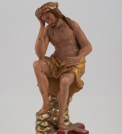 Zdjęcie nr 1: Rzeźba pełnoplastyczna, przyścienna, z tyłu ścięta, nieopracowana. Przedstawienie Chrystusa oczekującego na mękę, zwane Chrystus Frasobliwy lub Chrystus na zimnym głazie. Chrystus ukazany frontalnie, siedzi na niskiej skale, z rozsuniętymi kolanami, tułowiem przegiętym w prawą stronę i głową podpartą prawą ręką z łokciem wspartym na prawym kolanie Twarz okolona długimi, spływającymi na plecy włosami i zarostem. Na głowie korona cierniowa. Karnacja ciała z zaznaczonymi śladami męki. Na biodrach perizonium. U stóp Chrystusa leży krzyż. Rzeźba ustawiona na profilowanym postumencie.