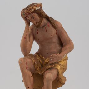 Zdjęcie nr 1: Rzeźba pełnoplastyczna, przyścienna, z tyłu ścięta, nieopracowana. Przedstawienie Chrystusa oczekującego na mękę, zwane Chrystus Frasobliwy lub Chrystus na zimnym głazie. Chrystus ukazany frontalnie, siedzi na niskiej skale, z rozsuniętymi kolanami, tułowiem przegiętym w prawą stronę i głową podpartą prawą ręką z łokciem wspartym na prawym kolanie Twarz okolona długimi, spływającymi na plecy włosami i zarostem. Na głowie korona cierniowa. Karnacja ciała z zaznaczonymi śladami męki. Na biodrach perizonium. U stóp Chrystusa leży krzyż. Rzeźba ustawiona na profilowanym postumencie.