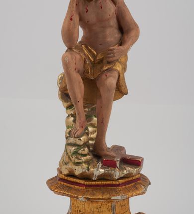 Zdjęcie nr 2: Rzeźba pełnoplastyczna, przyścienna, z tyłu ścięta, nieopracowana. Przedstawienie Chrystusa oczekującego na mękę, zwane Chrystus Frasobliwy lub Chrystus na zimnym głazie. Chrystus ukazany frontalnie, siedzi na niskiej skale, z rozsuniętymi kolanami, tułowiem przegiętym w prawą stronę i głową podpartą prawą ręką z łokciem wspartym na prawym kolanie Twarz okolona długimi, spływającymi na plecy włosami i zarostem. Na głowie korona cierniowa. Karnacja ciała z zaznaczonymi śladami męki. Na biodrach perizonium. U stóp Chrystusa leży krzyż. Rzeźba ustawiona na profilowanym postumencie.