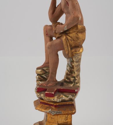 Zdjęcie nr 3: Rzeźba pełnoplastyczna, przyścienna, z tyłu ścięta, nieopracowana. Przedstawienie Chrystusa oczekującego na mękę, zwane Chrystus Frasobliwy lub Chrystus na zimnym głazie. Chrystus ukazany frontalnie, siedzi na niskiej skale, z rozsuniętymi kolanami, tułowiem przegiętym w prawą stronę i głową podpartą prawą ręką z łokciem wspartym na prawym kolanie Twarz okolona długimi, spływającymi na plecy włosami i zarostem. Na głowie korona cierniowa. Karnacja ciała z zaznaczonymi śladami męki. Na biodrach perizonium. U stóp Chrystusa leży krzyż. Rzeźba ustawiona na profilowanym postumencie.